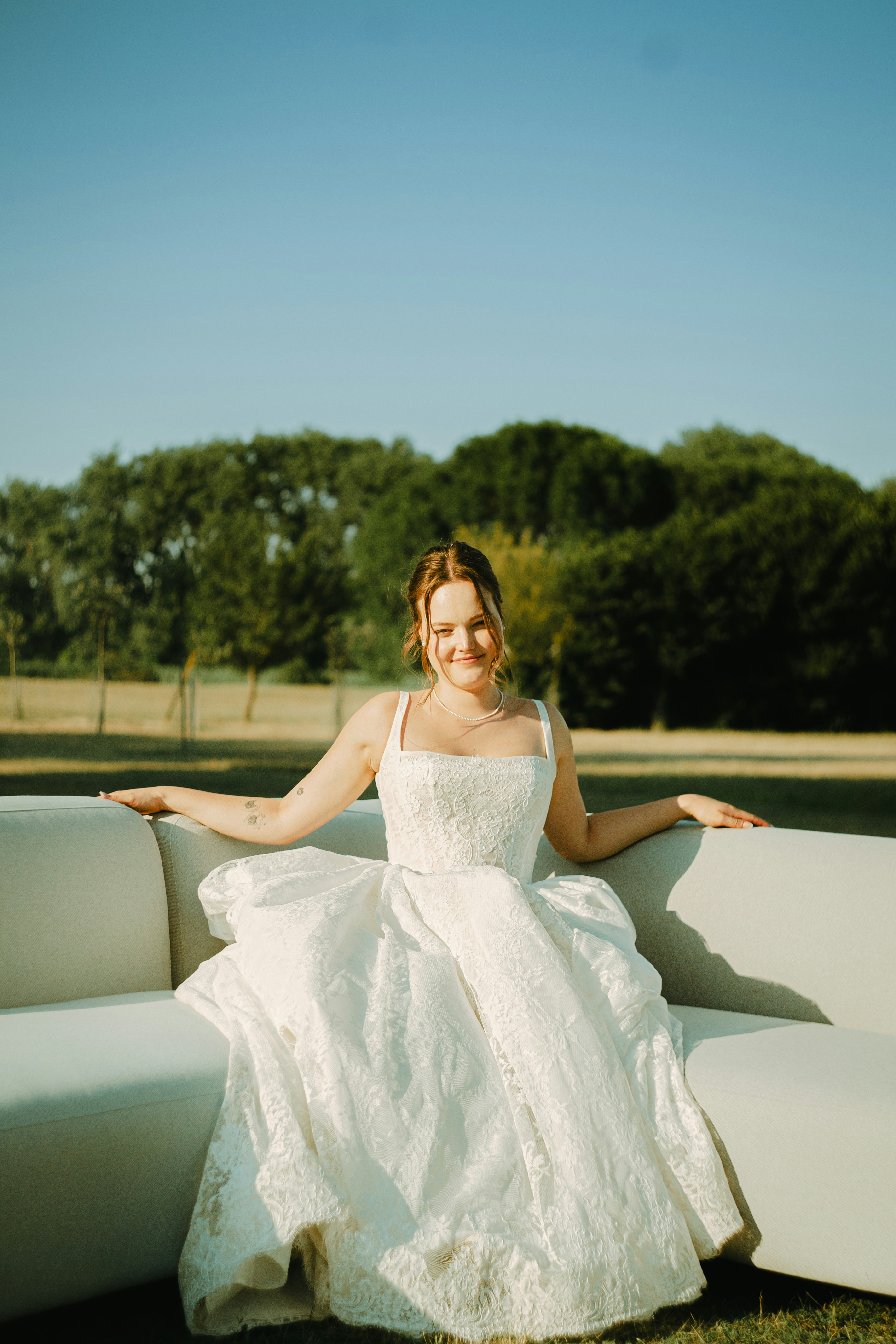 A woman in a white lace wedding dress on a sofa outdoors