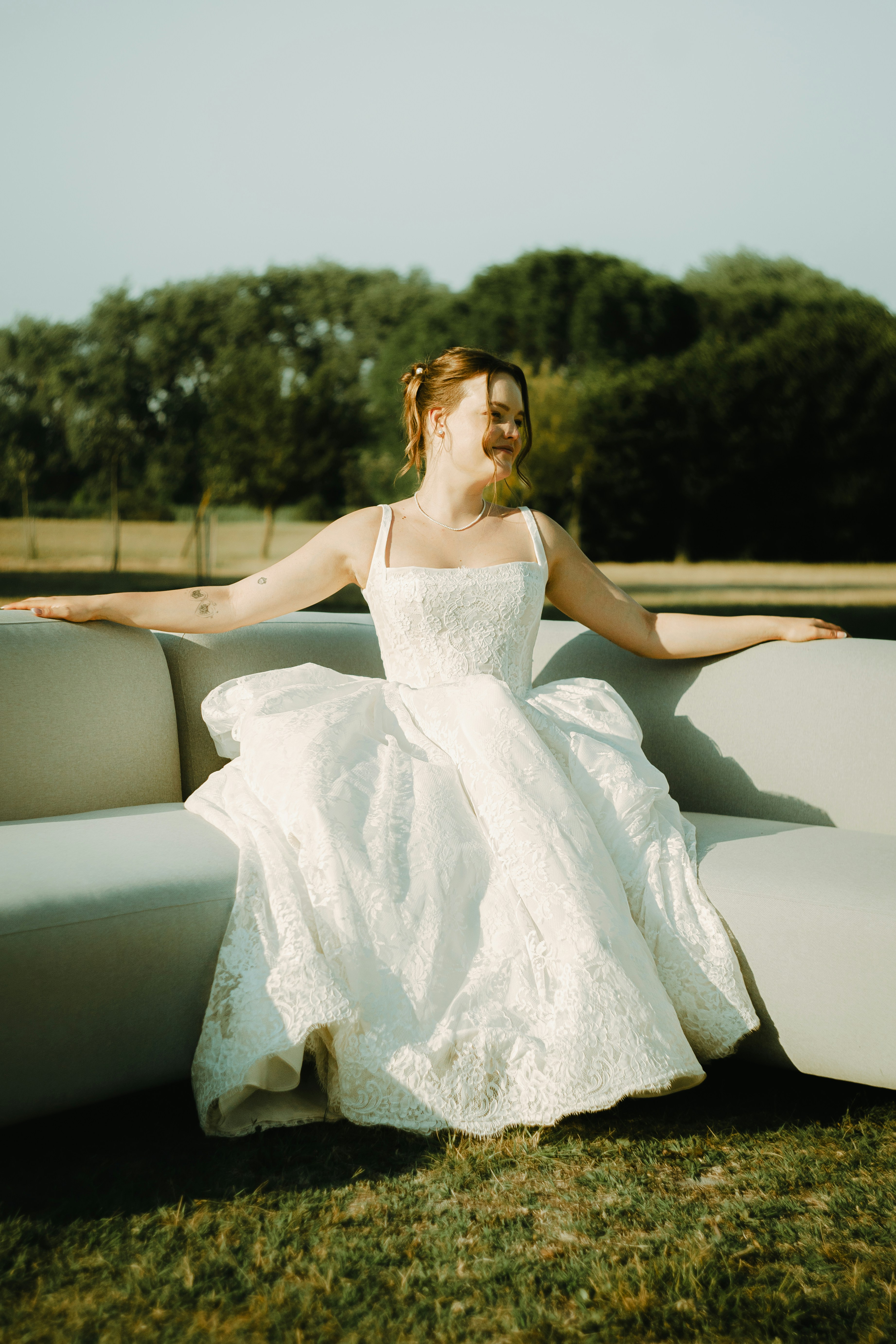A woman in a white lace wedding dress on a sofa in a park