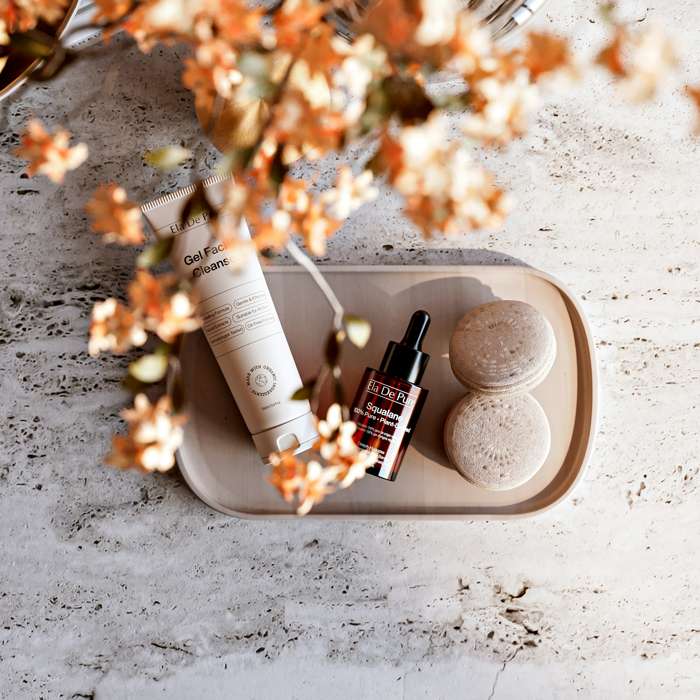 A facial cleanser tube, a serum bottle, and two sponges on a tray
