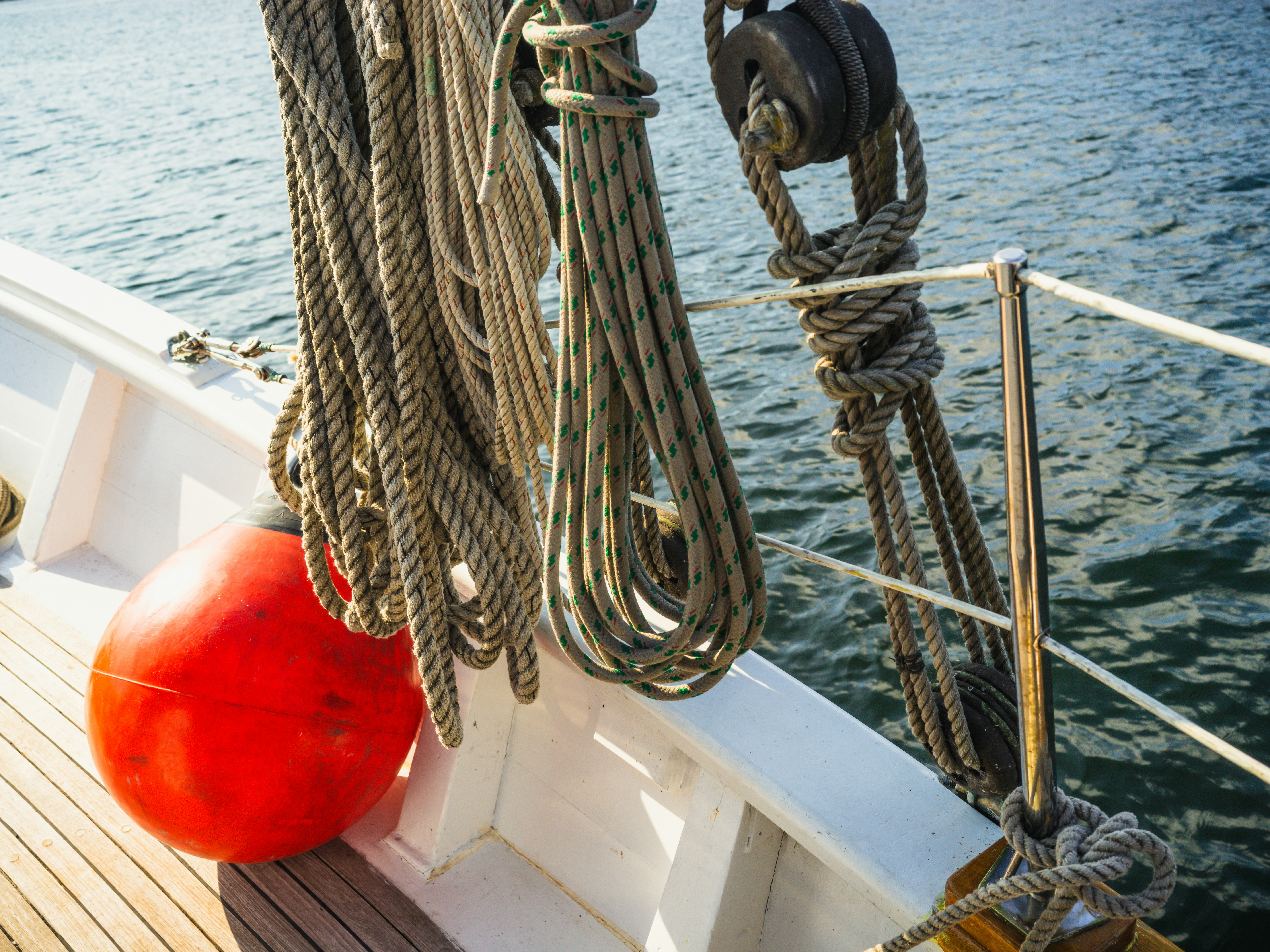 Coiled nautical ropes and a red fender on a wooden boat deck