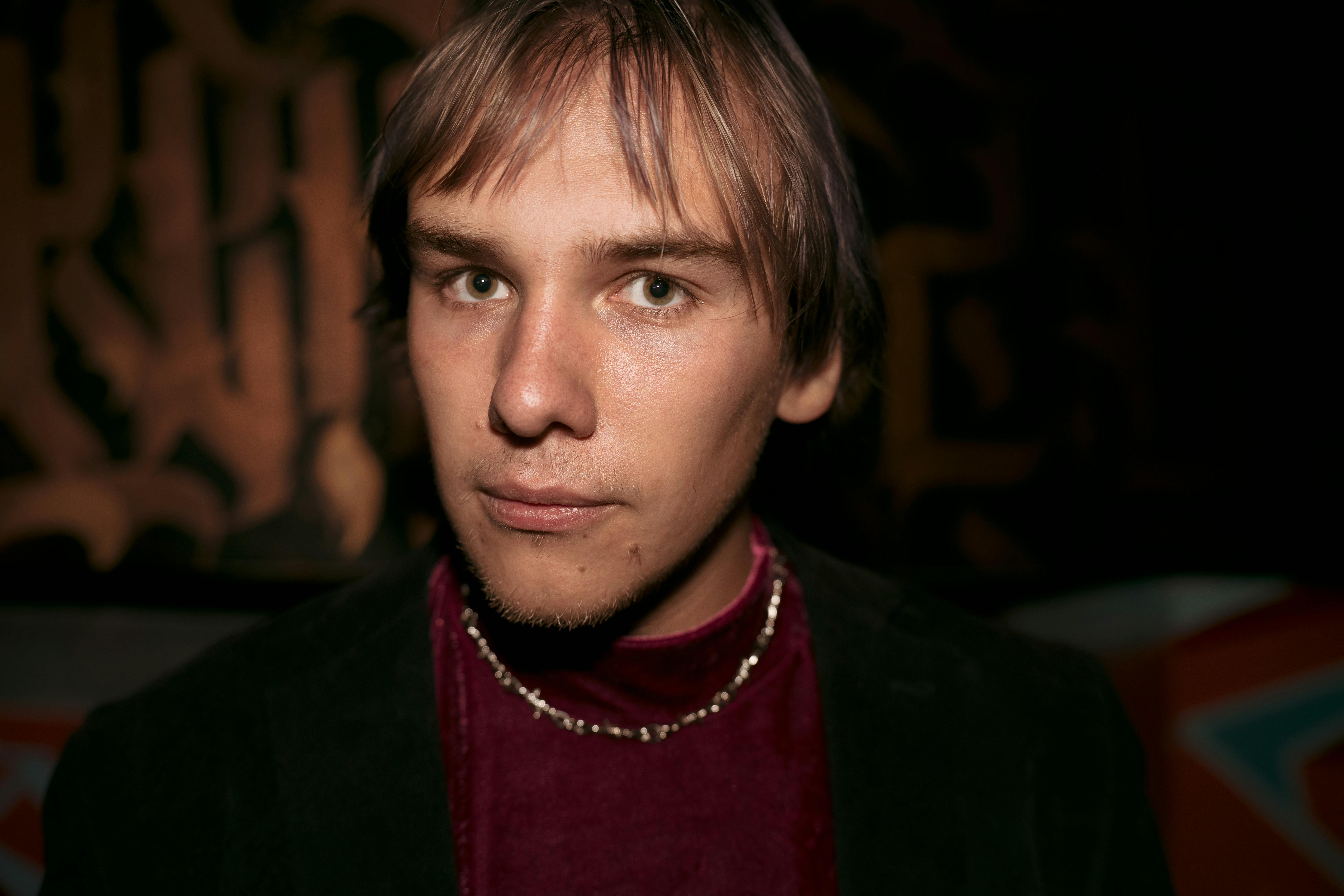 A person with light brown hair wearing a maroon turtleneck and dark jacket