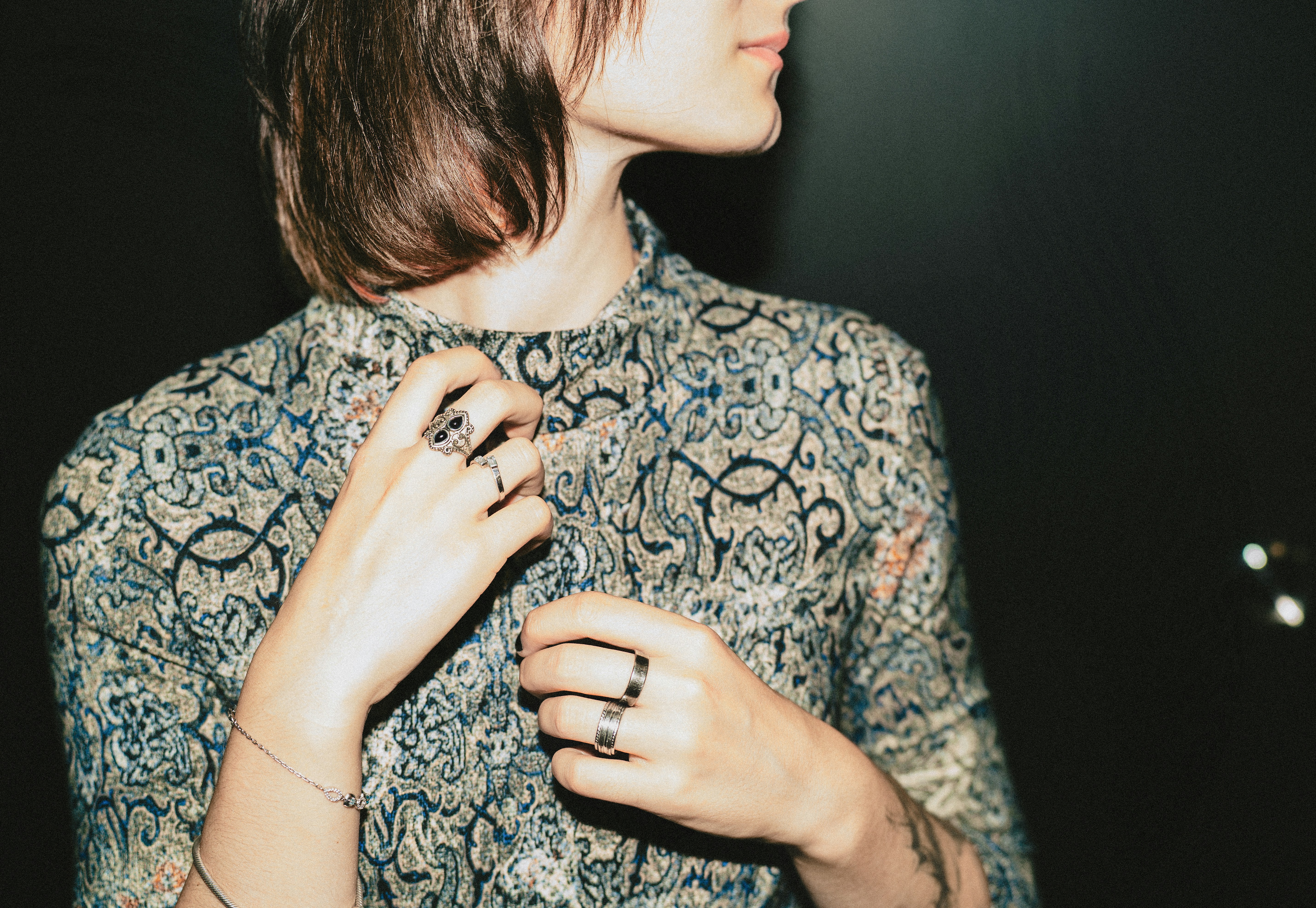 A person in a patterned shirt adjusting their collar with rings on their fingers