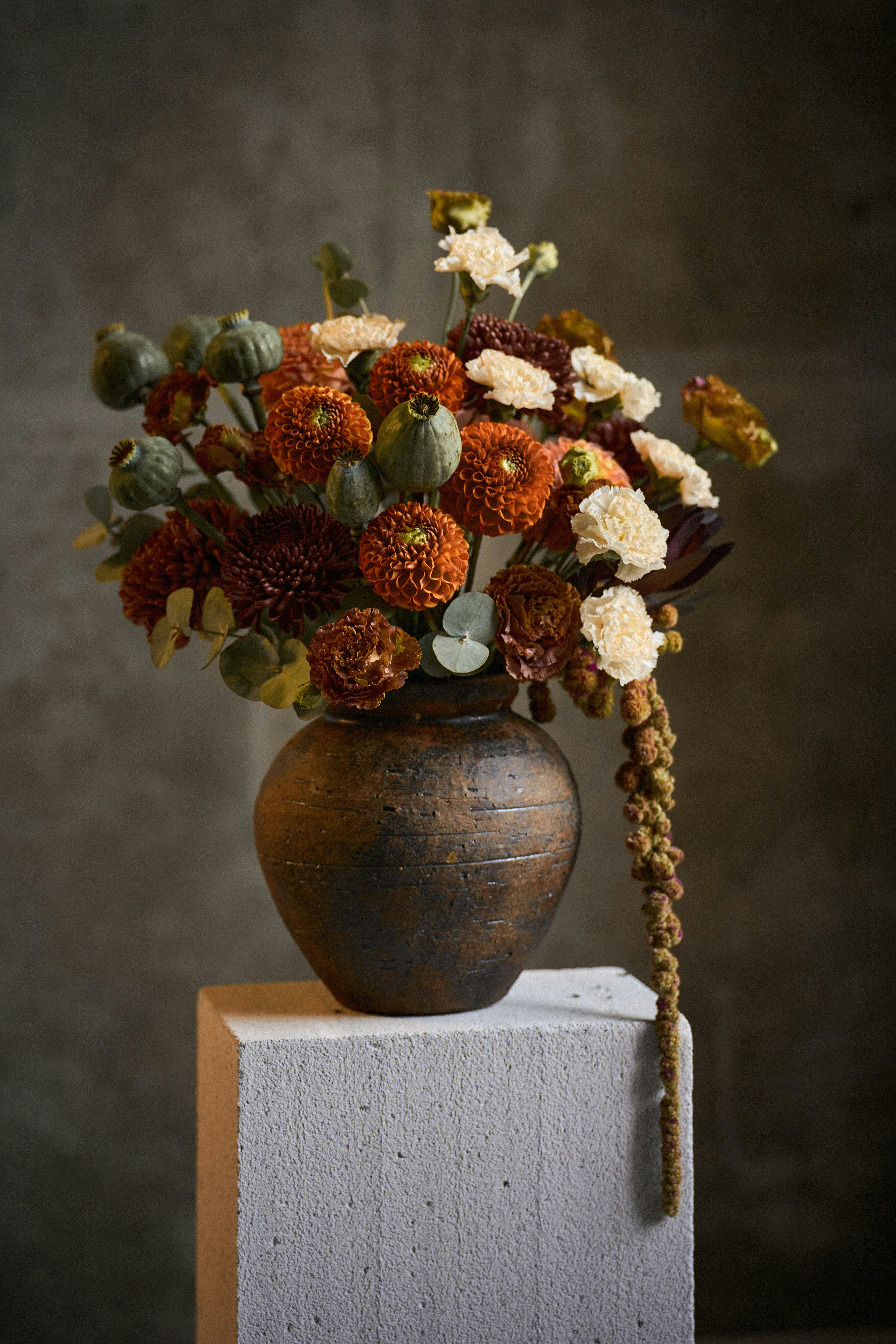A bouquet of orange dahlias and green poppy pods in a rustic ceramic vase