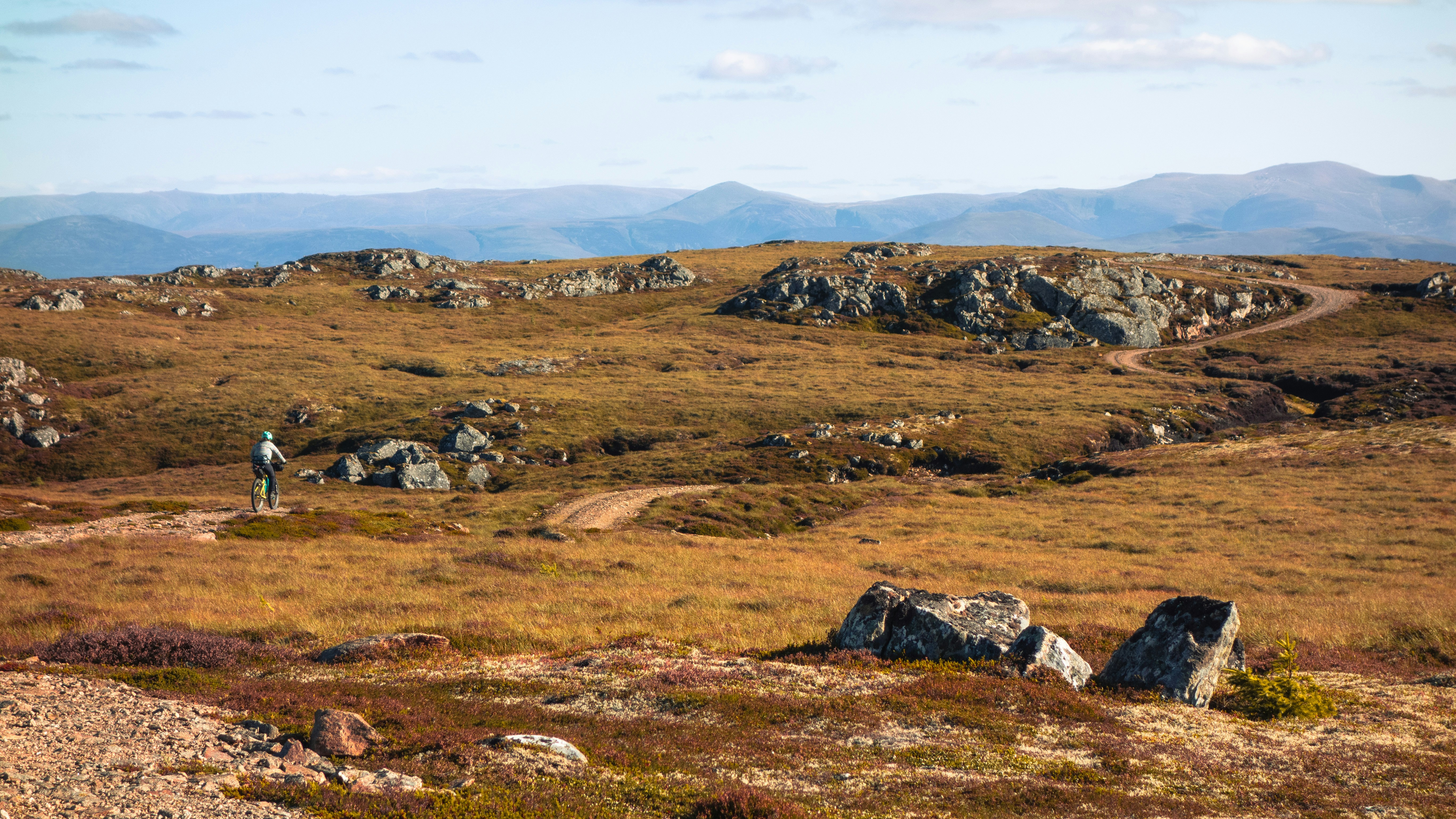 A person cycling on a dirt path through a rocky tundra landscape