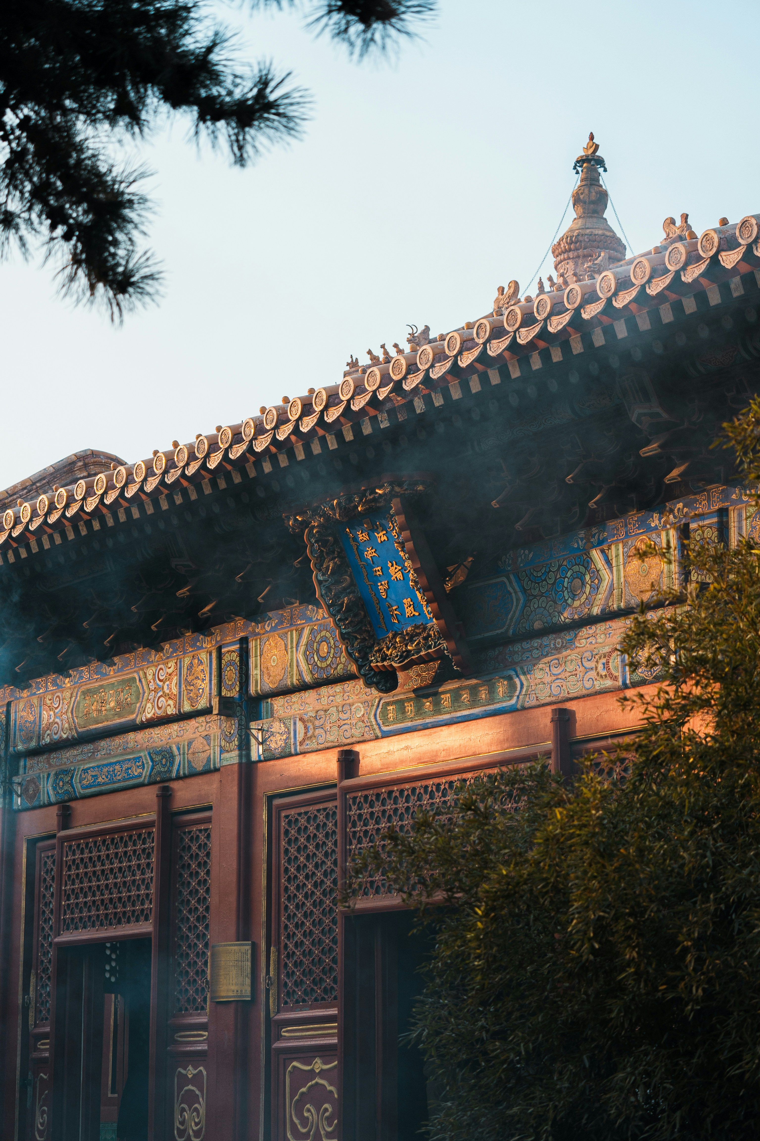 Ornate roof of a traditional Chinese temple with blue signage and incense smoke