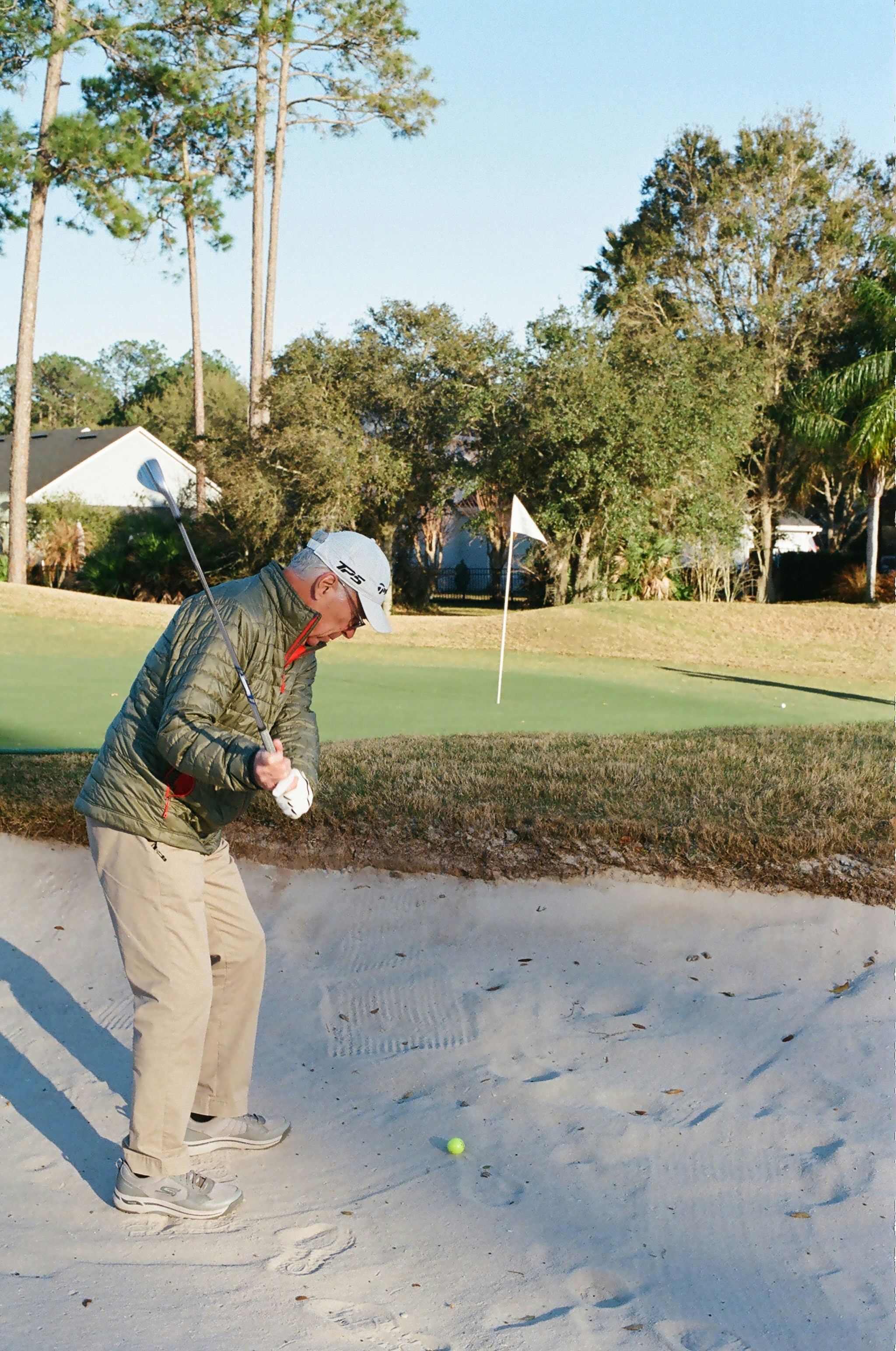 An adult golfer swinging a club in a sand bunker on a golf course