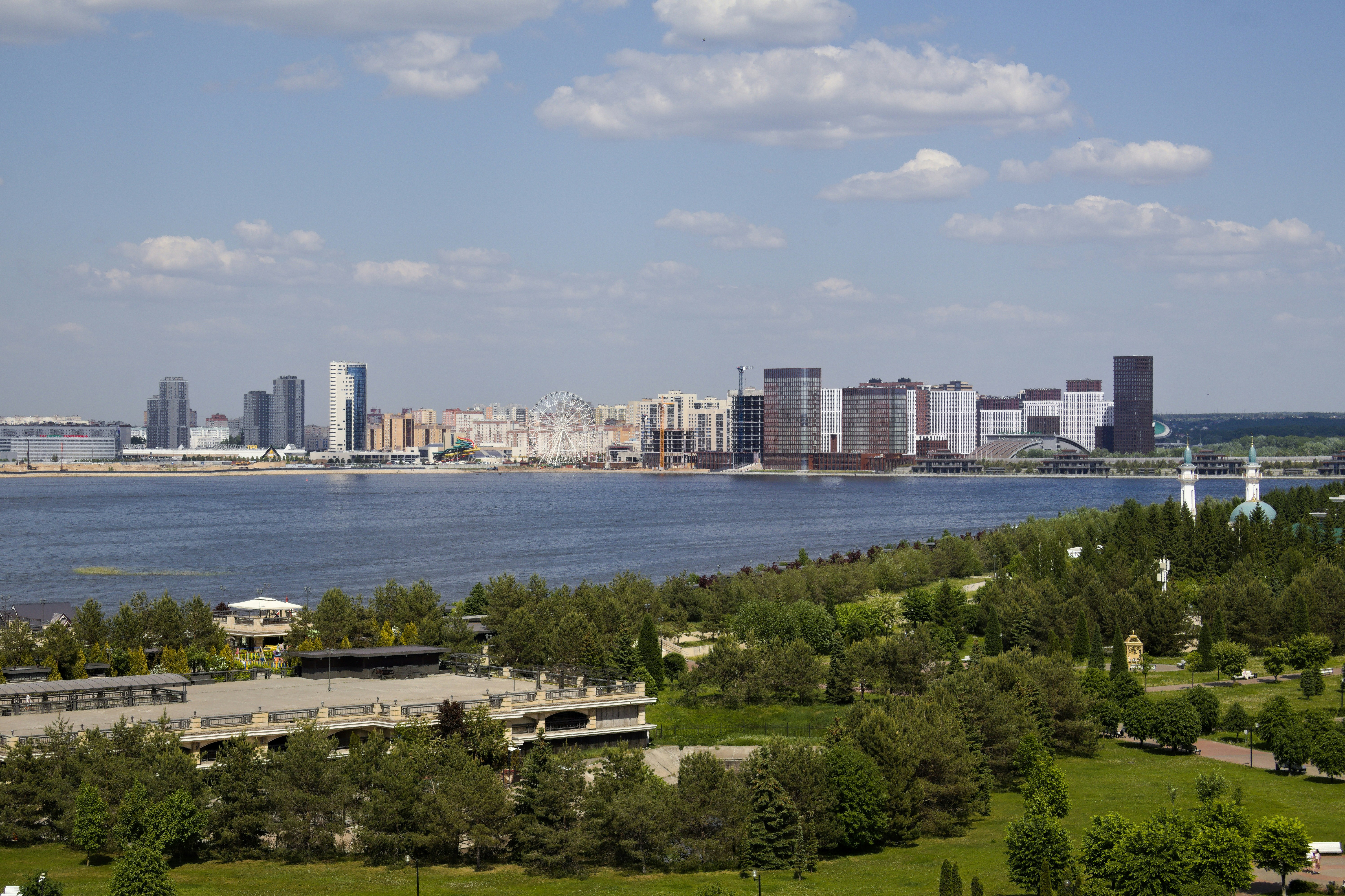 A city skyline with a ferris wheel across a wide river and parkland