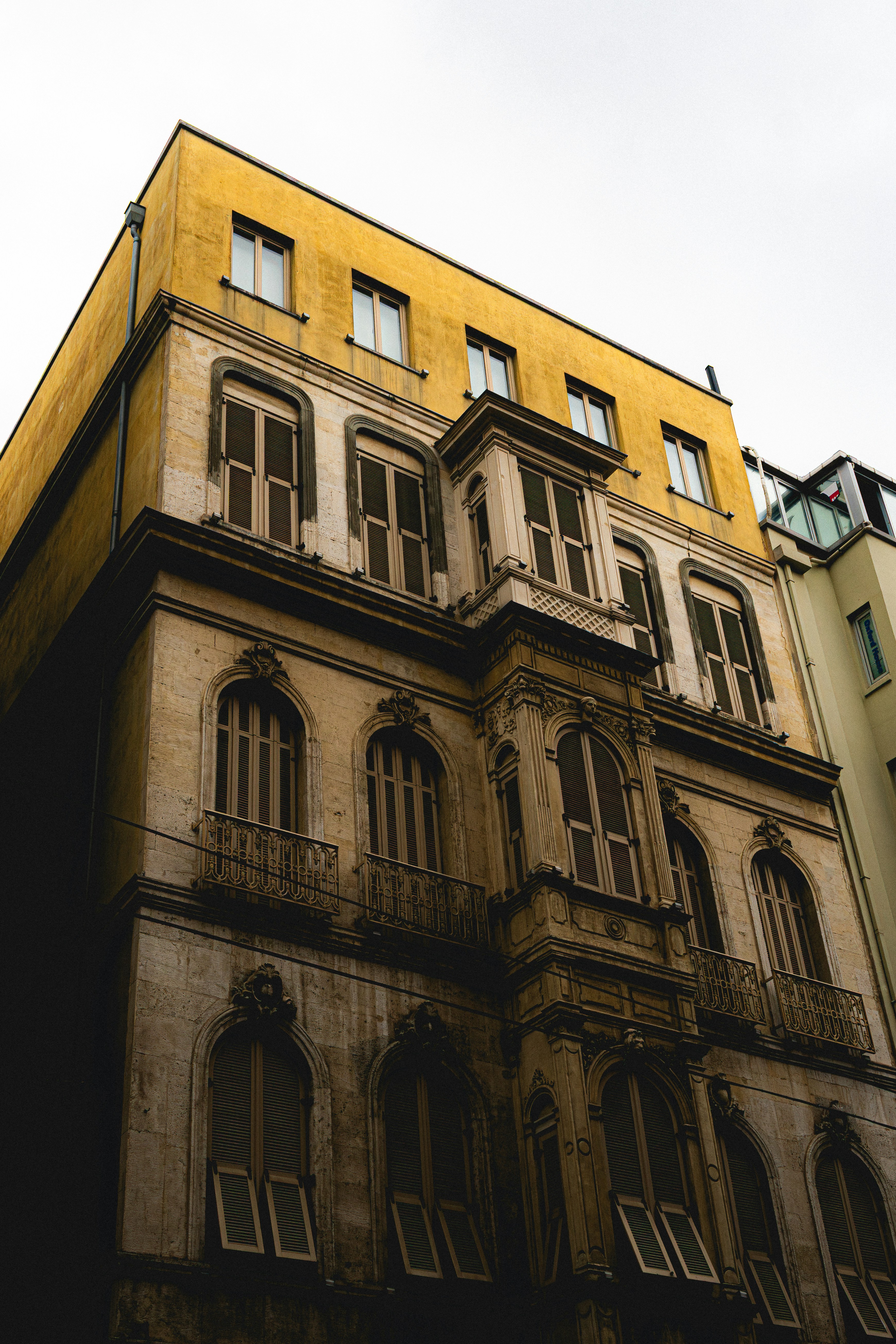 A historic stone building with a yellow upper facade and arched windows