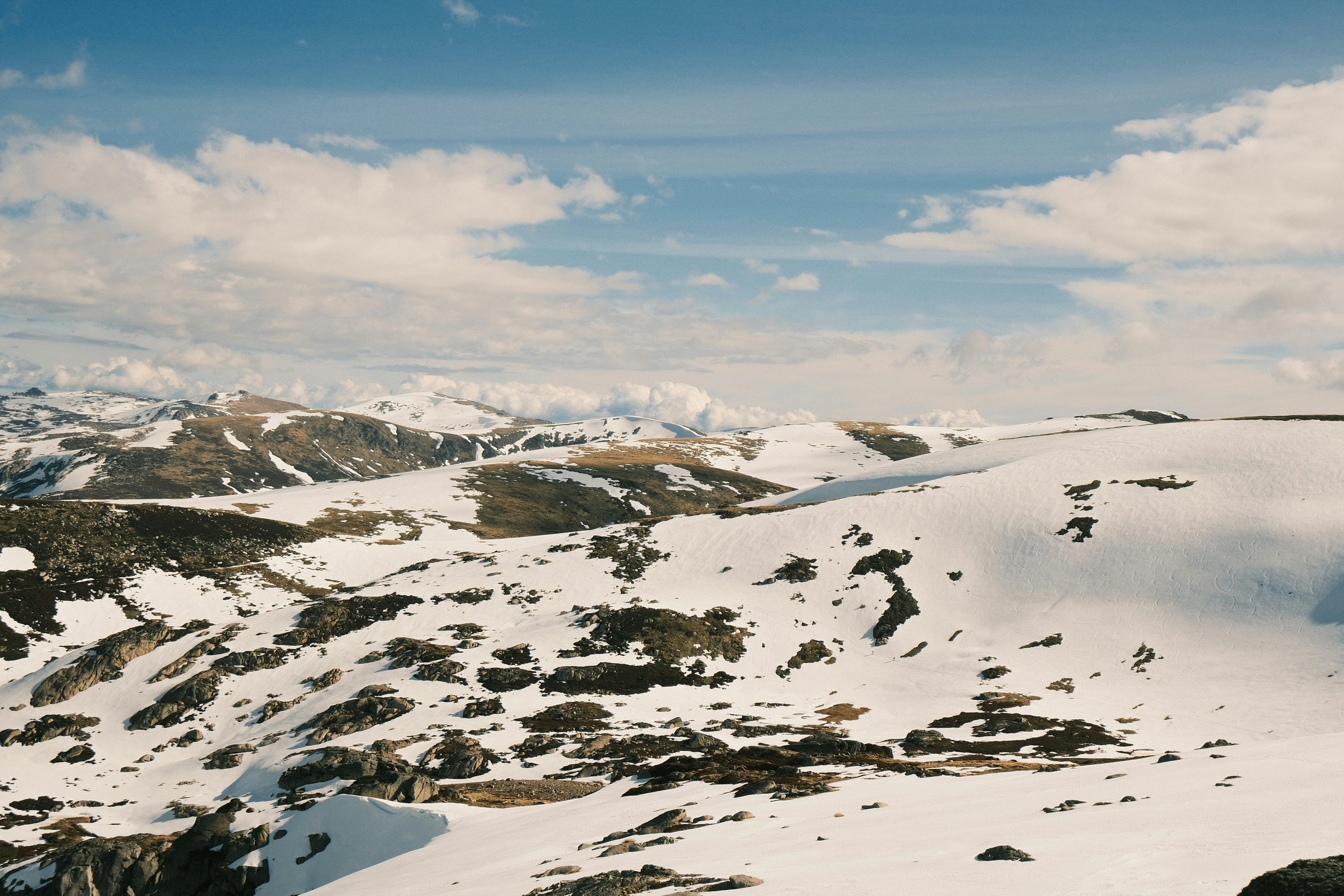 Snowy rolling hills under a blue sky with scattered white clouds