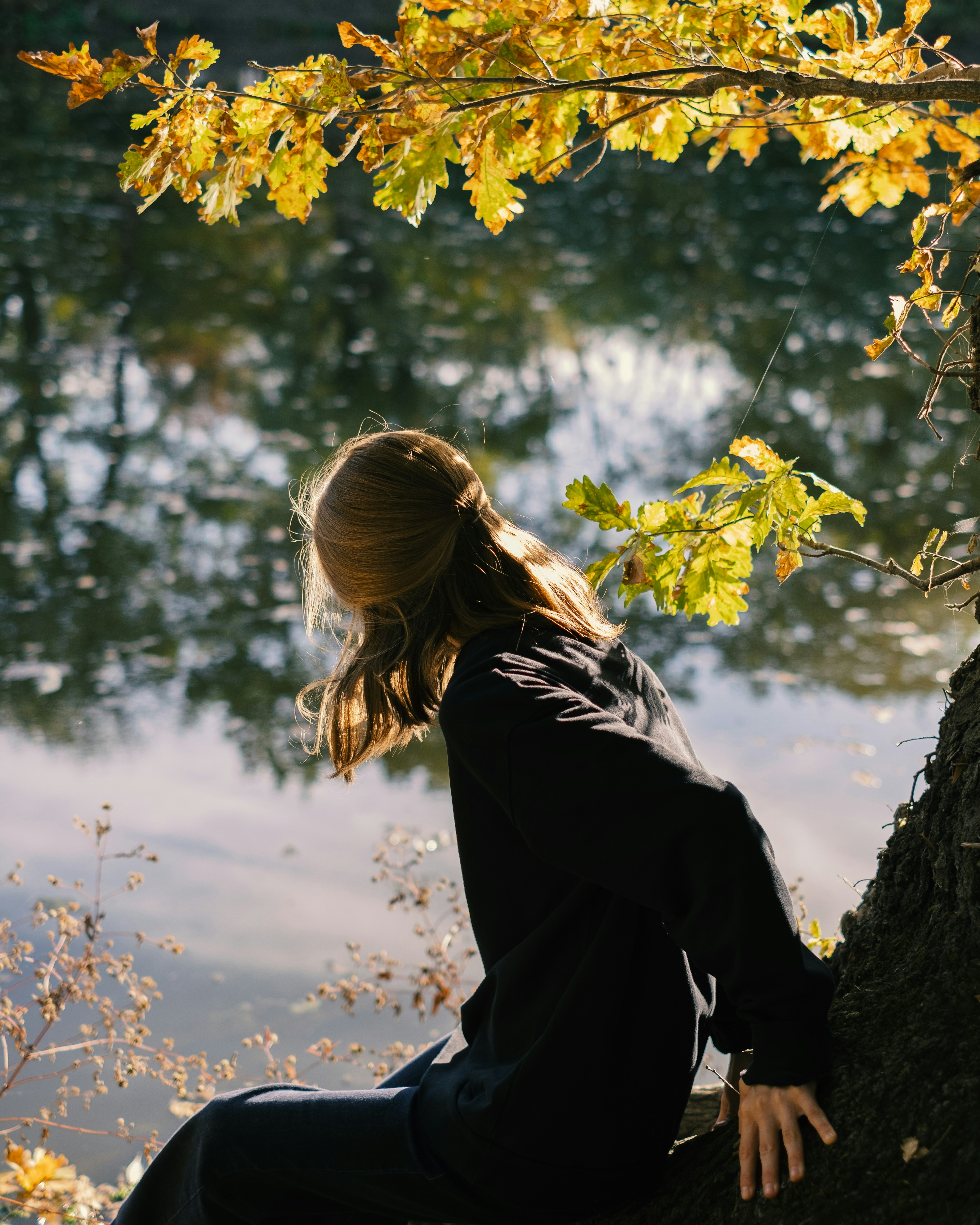 A woman in a black sweatshirt by water under yellow oak leaves