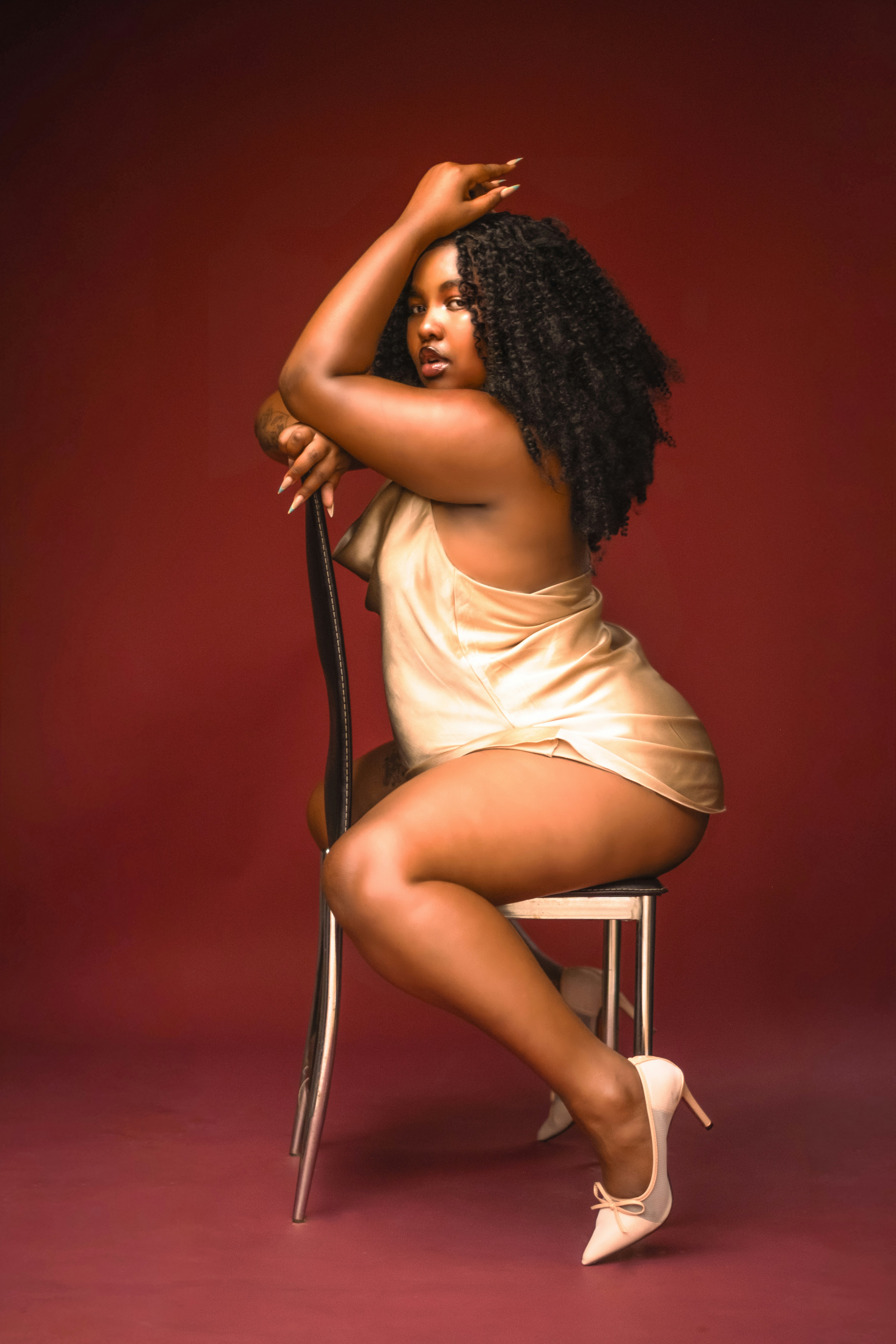 A woman in a gold satin dress sitting on a chair against a red background