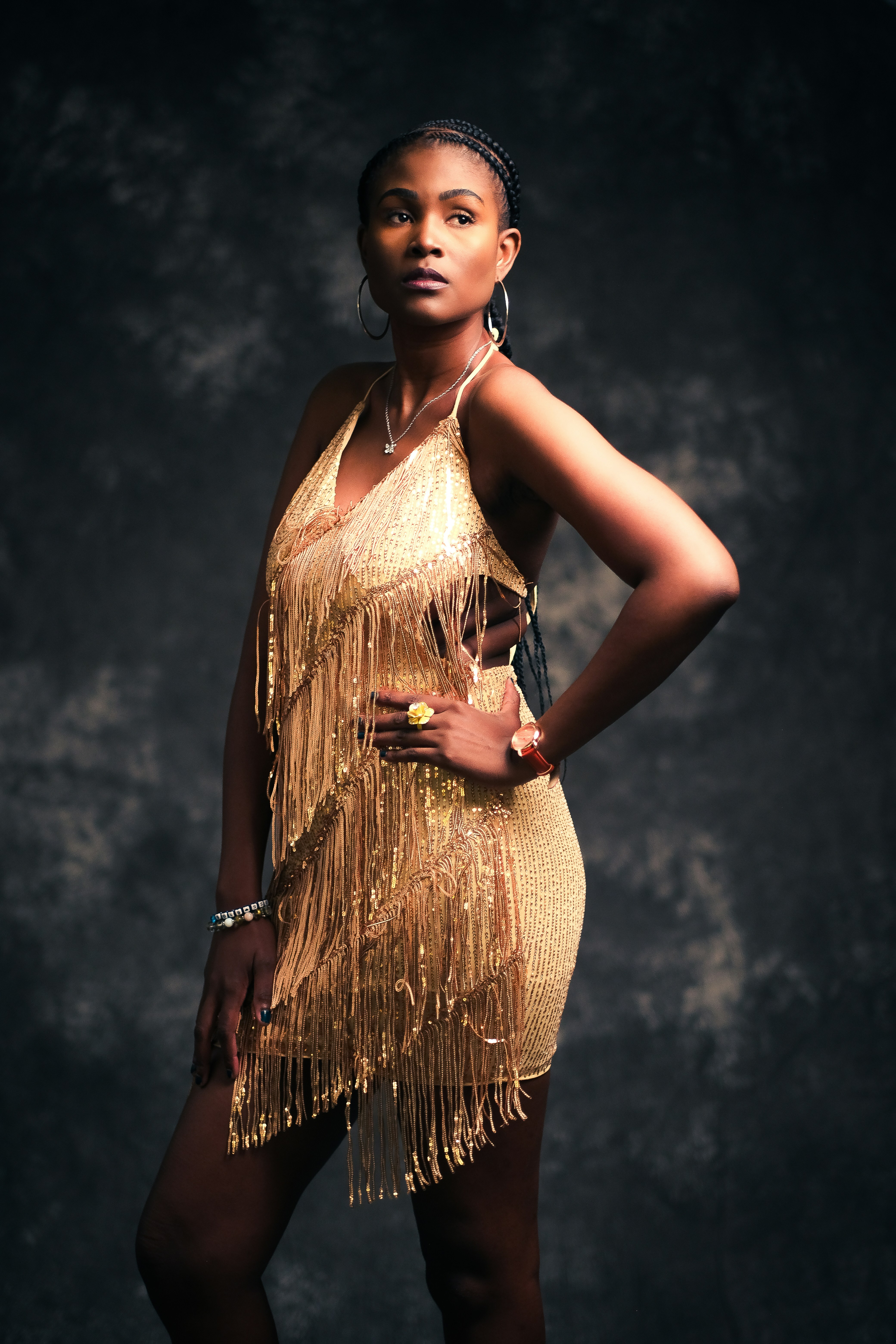 A woman in a gold fringed dress posing against a dark textured background