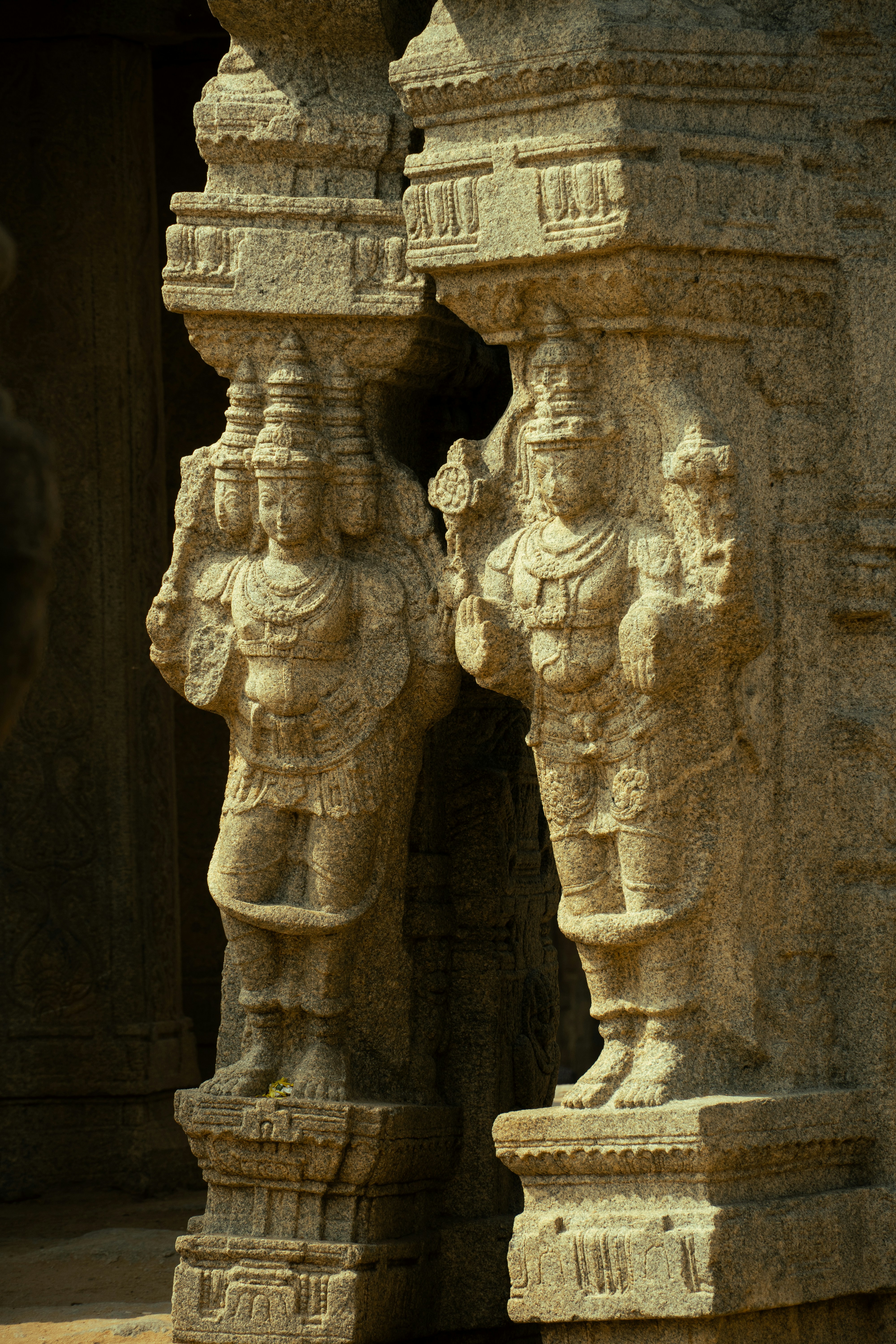 Two stone carved figures on ornate pillars in a temple