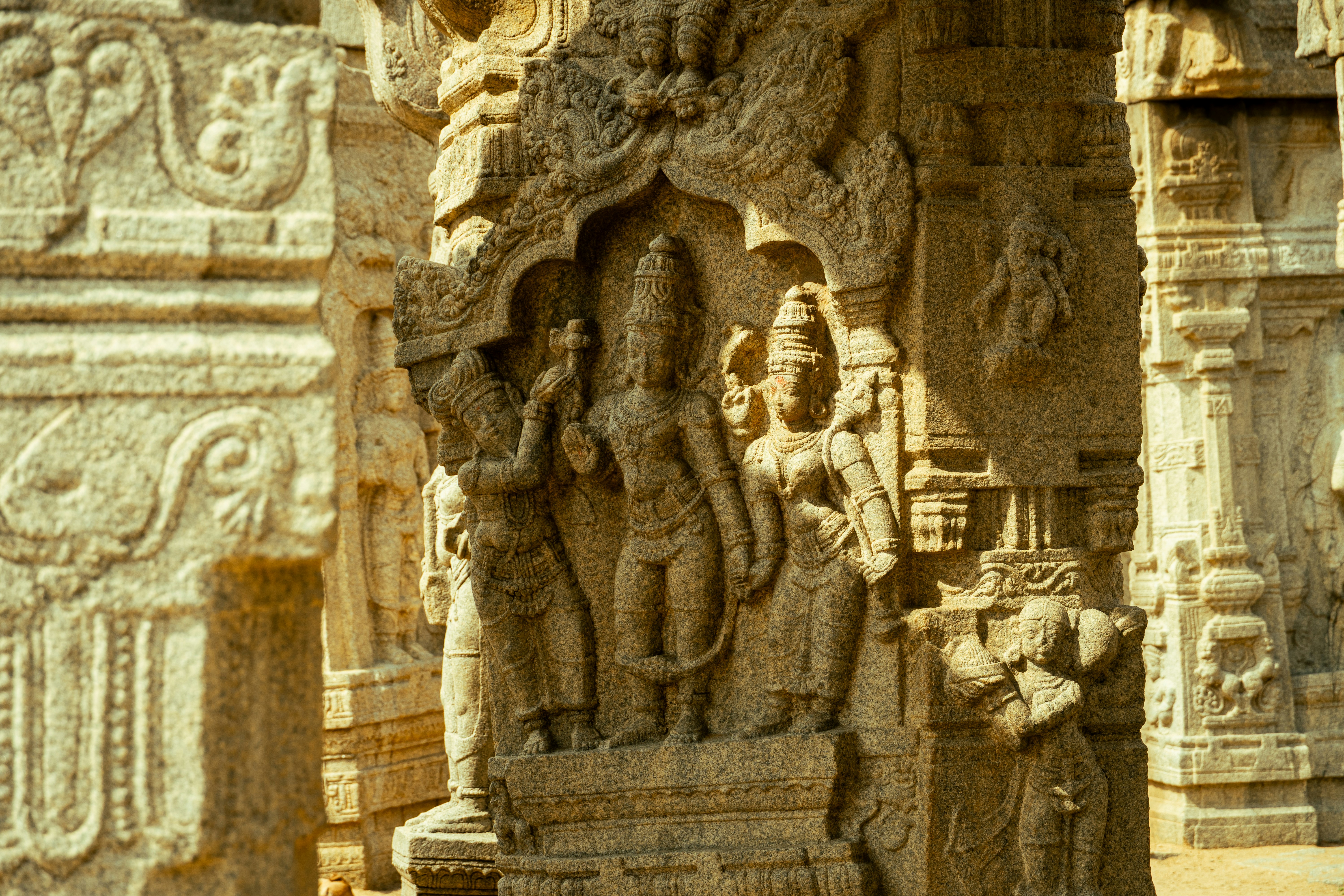 Intricate stone carvings of figures on a temple pillar in warm sunlight