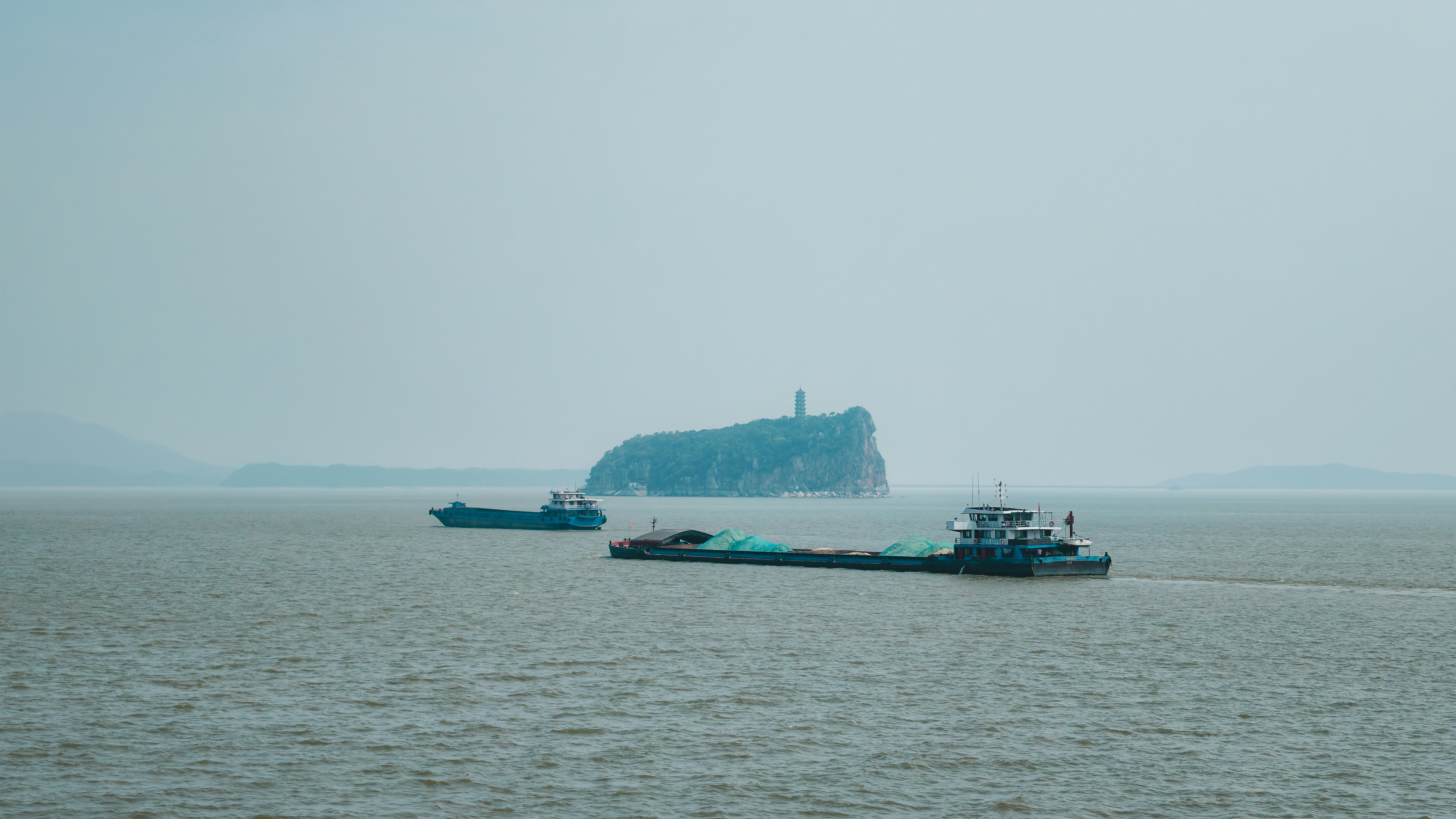 Two cargo ships on a wide river near a small island with a pagoda