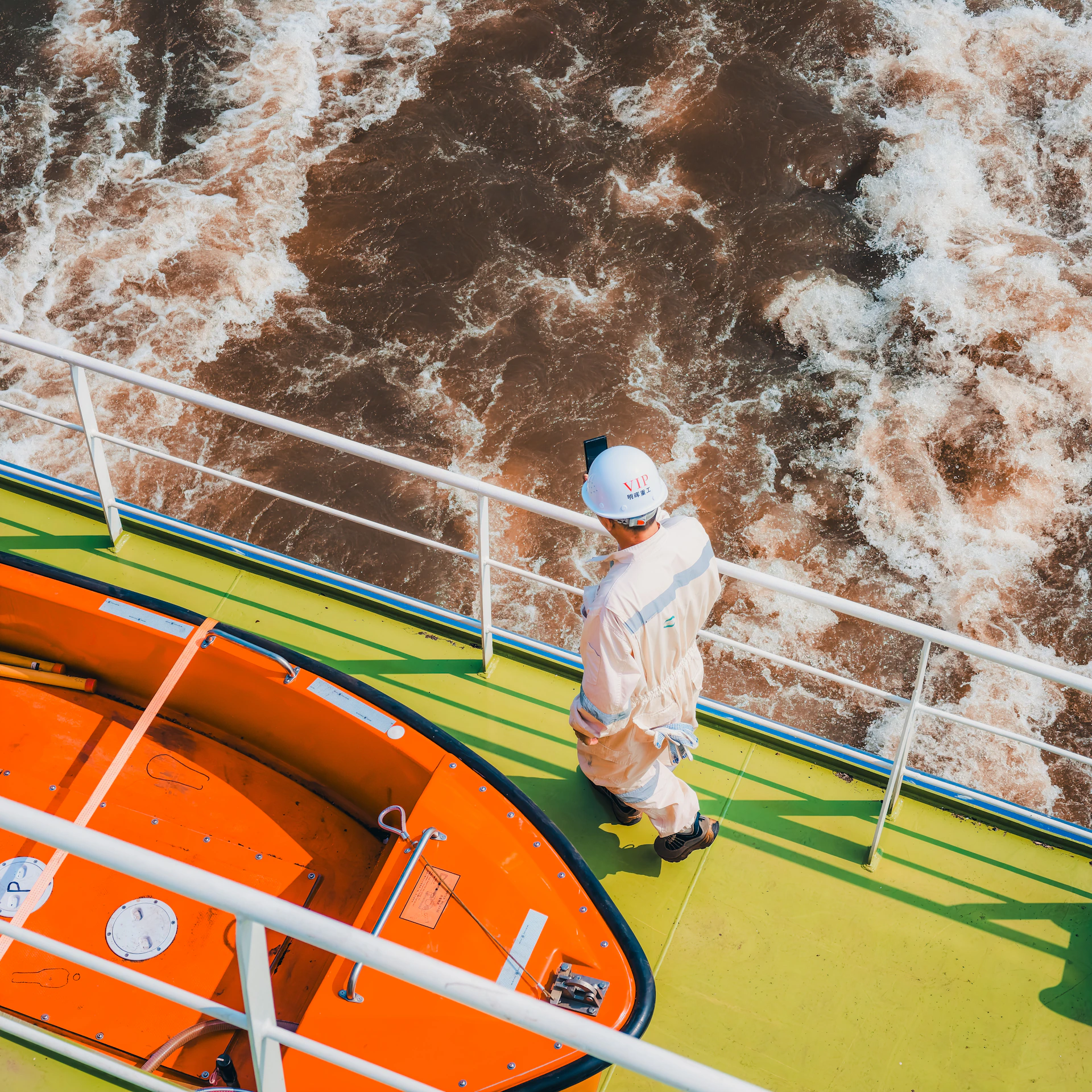 A person in a white hard hat and coveralls on a ship deck