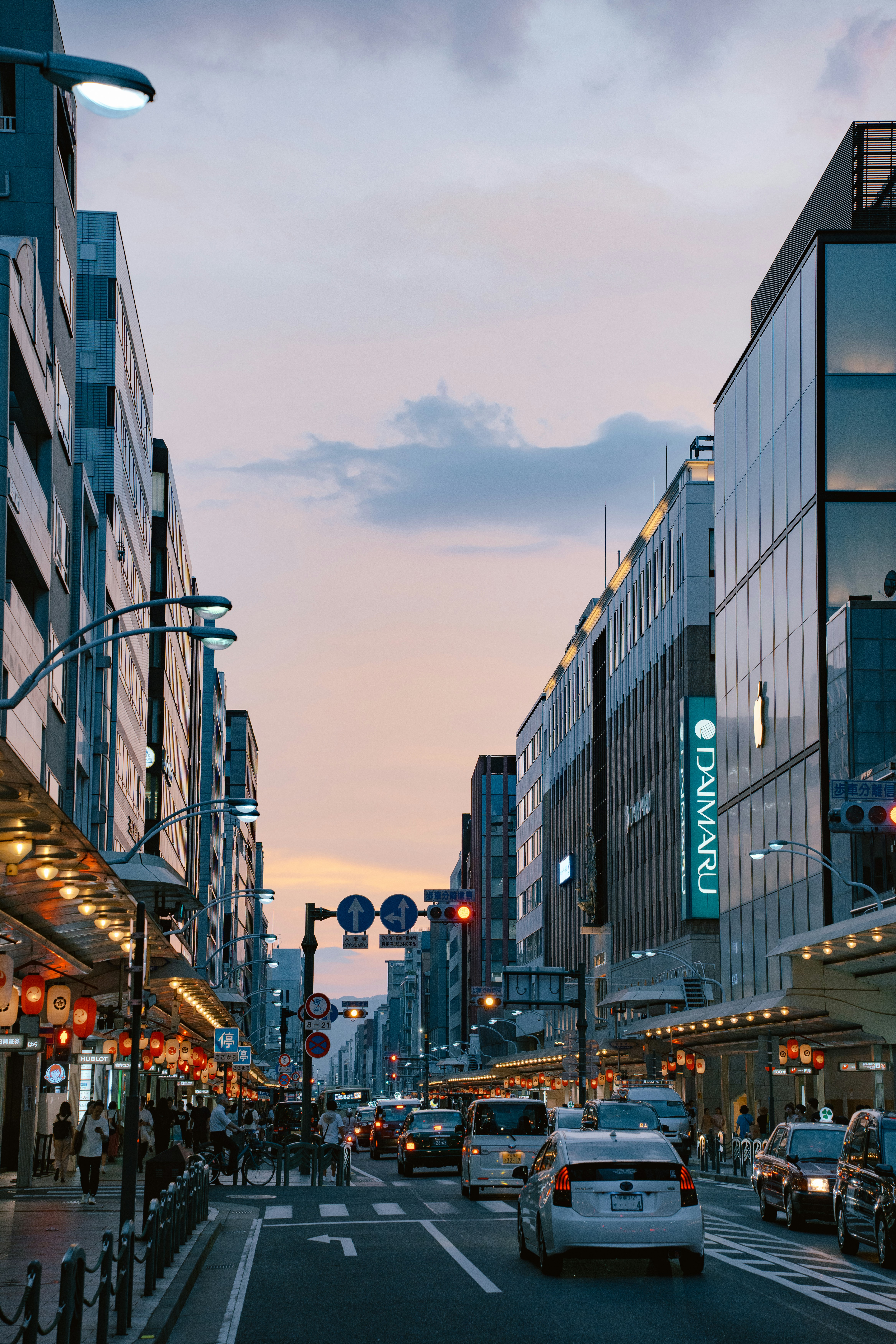 Cars driving down a city street lined with tall buildings and glowing lanterns