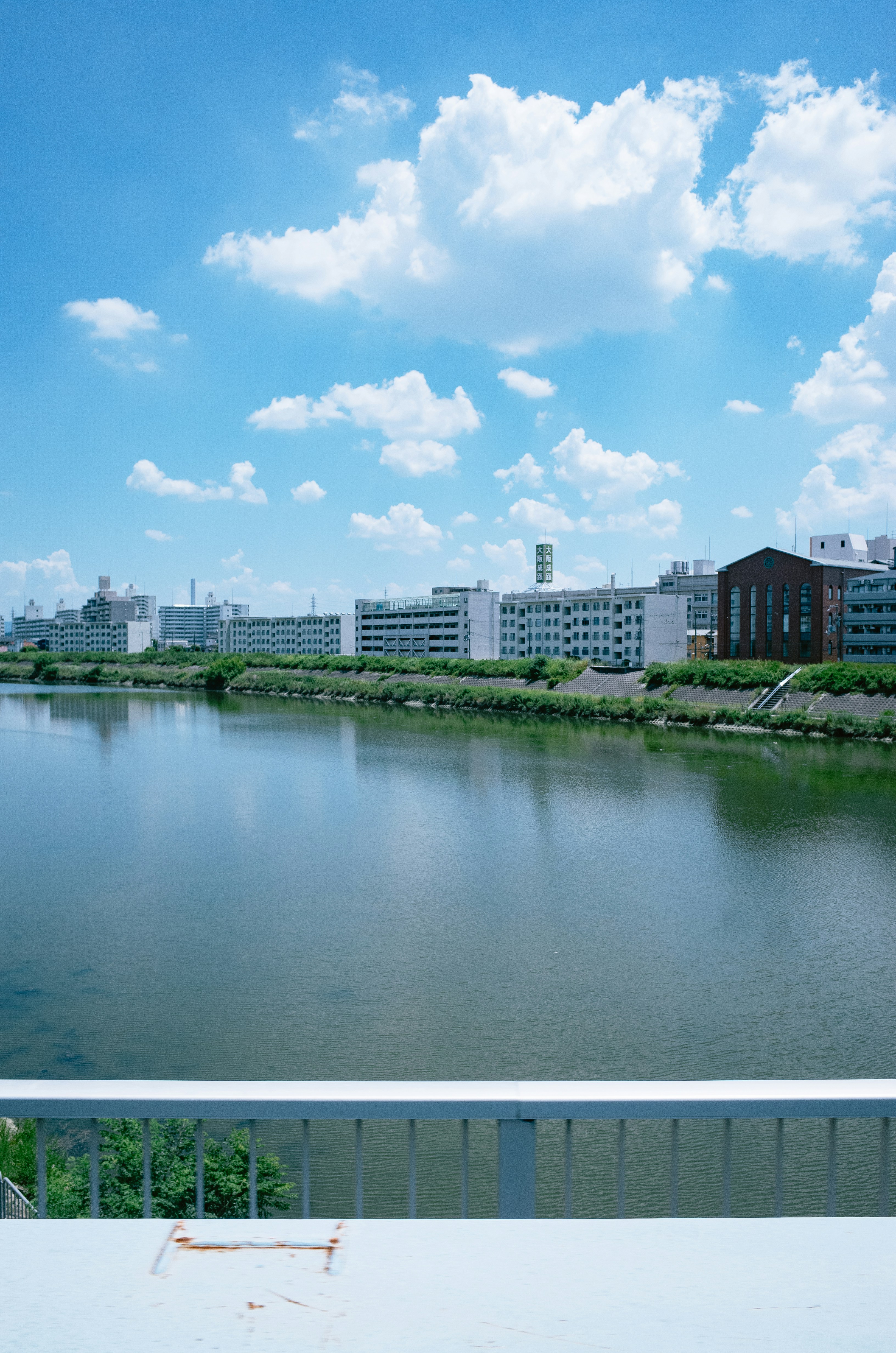 A wide river flowing past apartment buildings under a bright blue sky