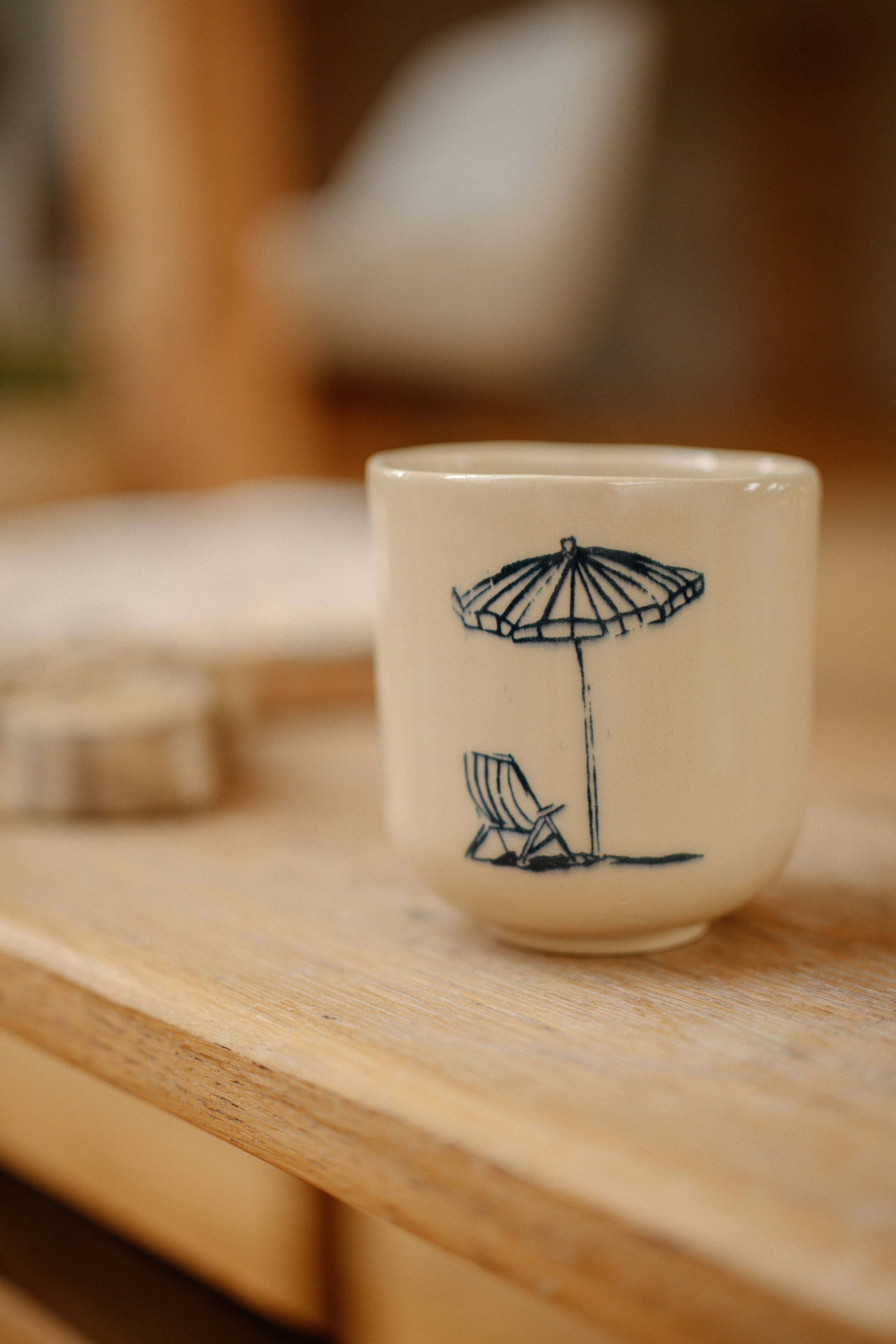 A ceramic cup with a blue ink drawing of a beach umbrella and chair