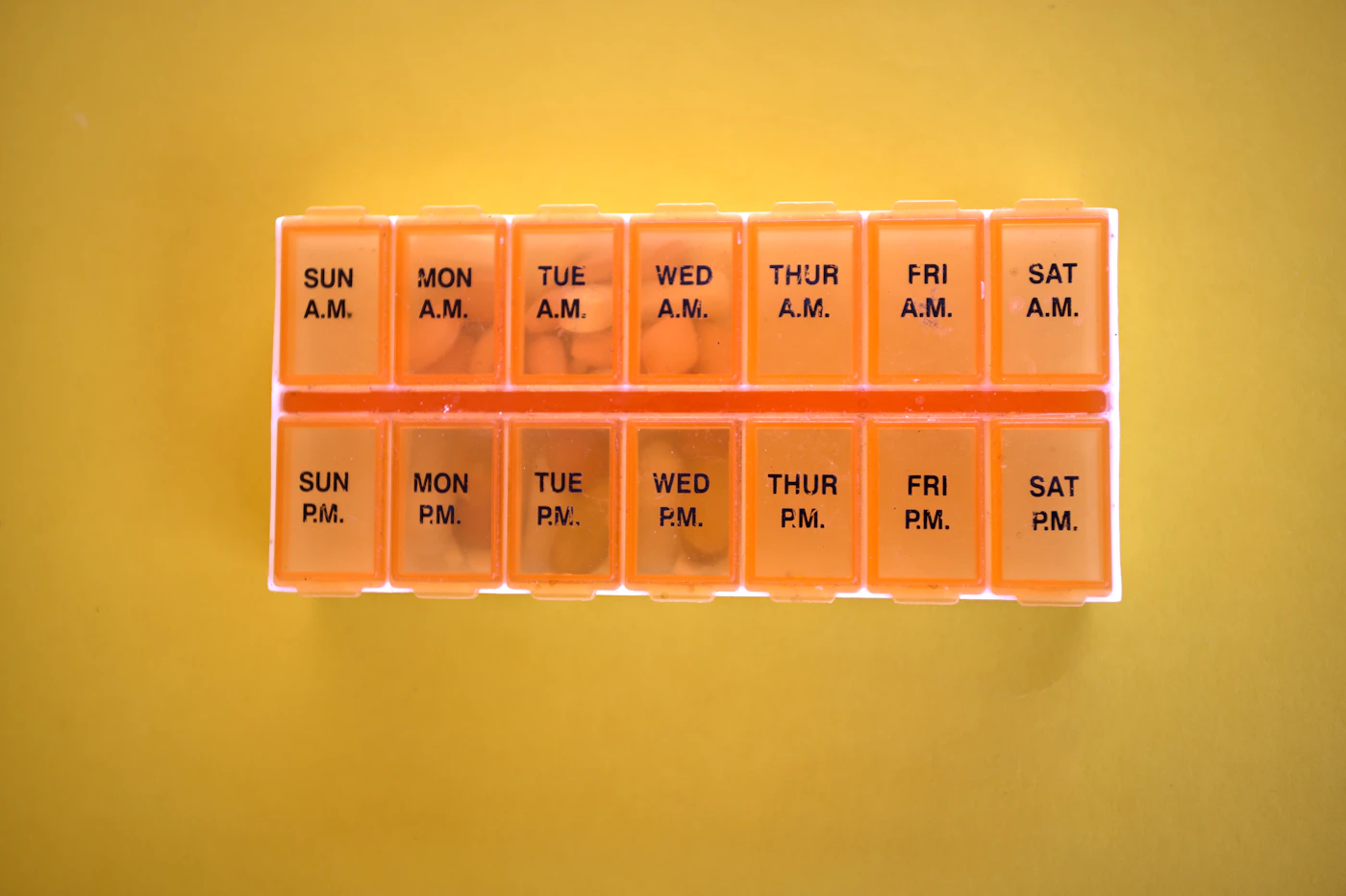 Porta-comprimidos semanal laranja com compartimentos de manhã e noite sobre fundo amarelo — escolha de tratamento na SOP
