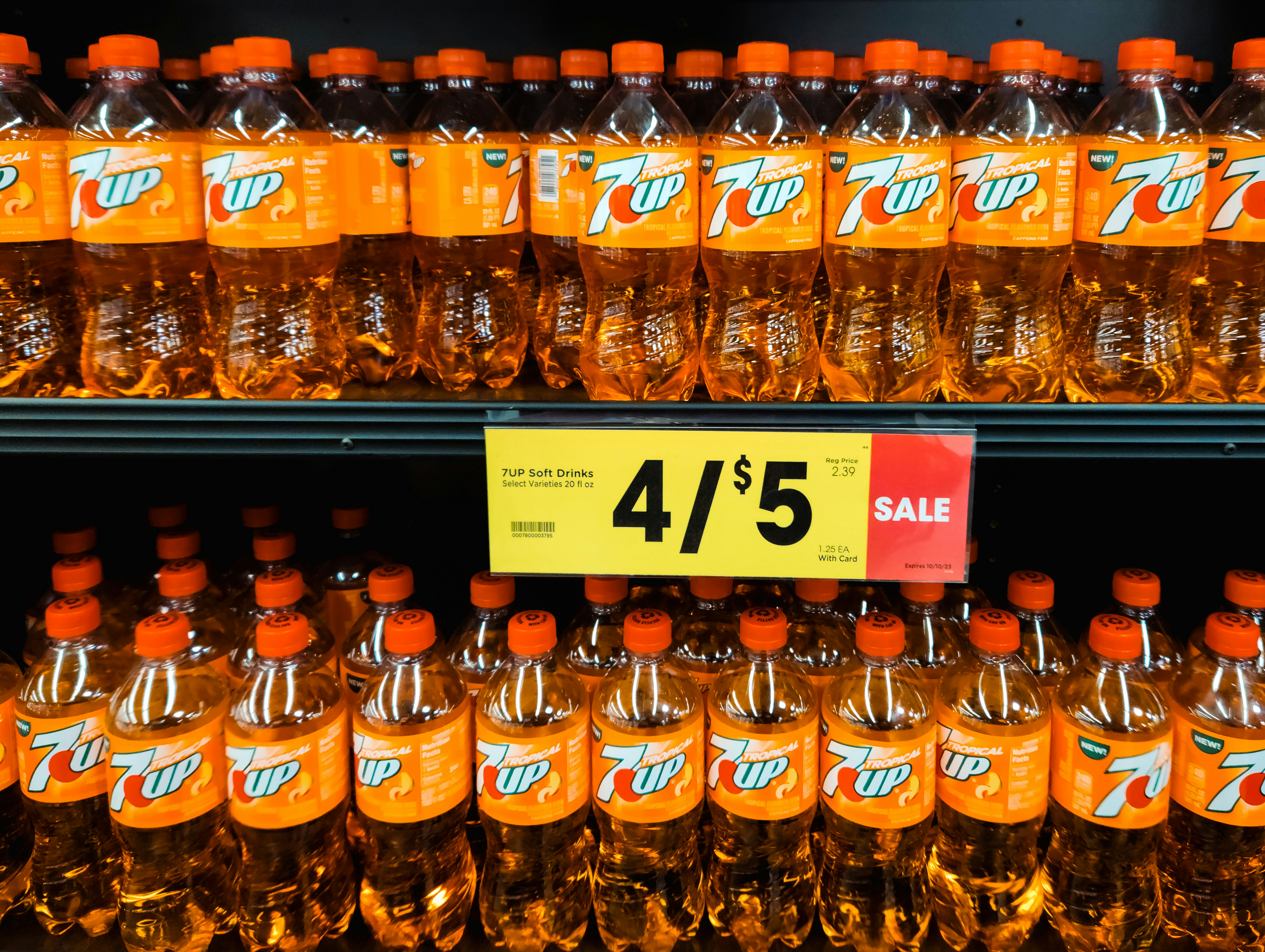 Rows of plastic bottles of Tropical 7up on store shelves with a sale sign