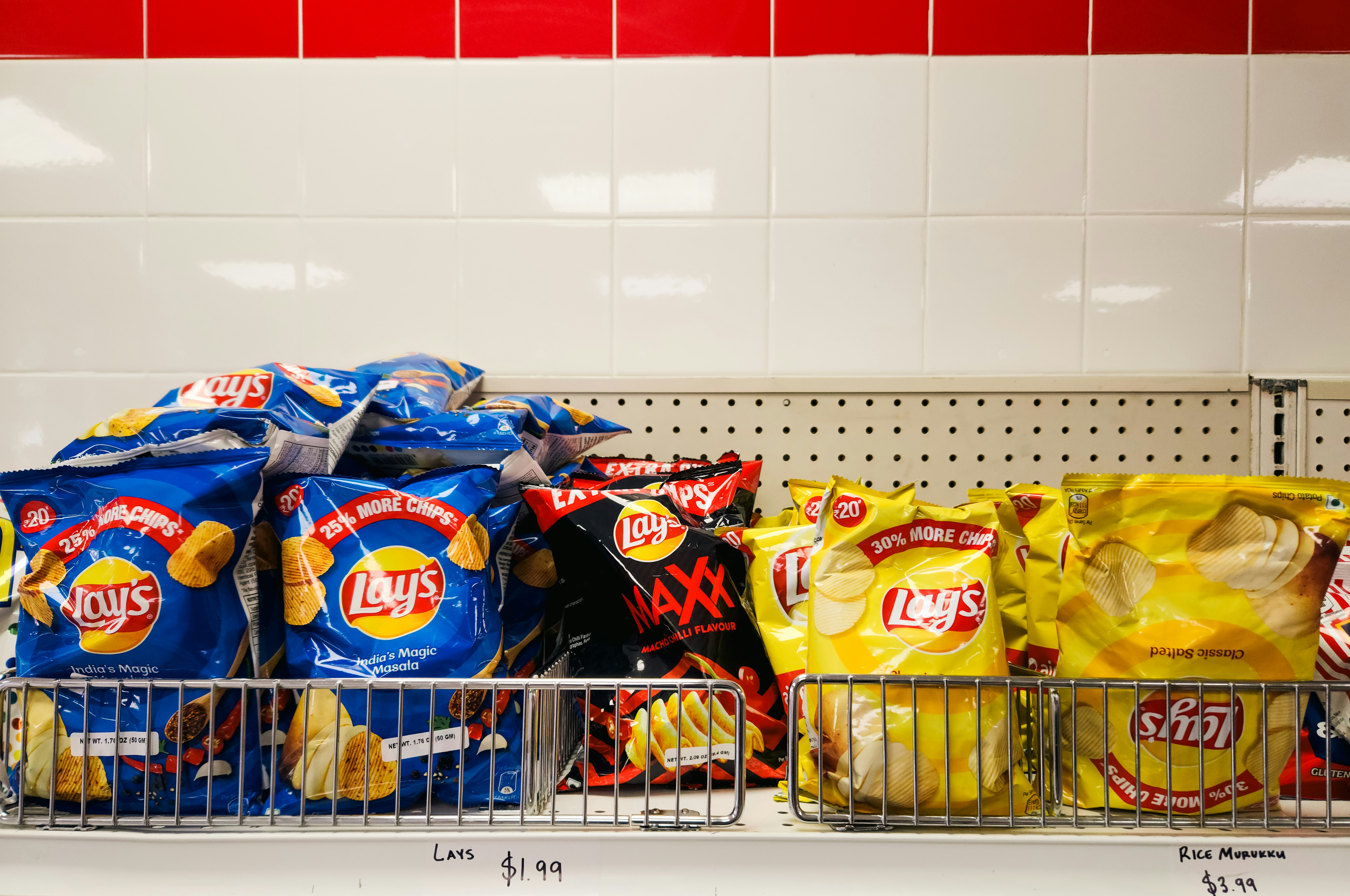 Bags of potato chips on a store shelf against a white tiled wall