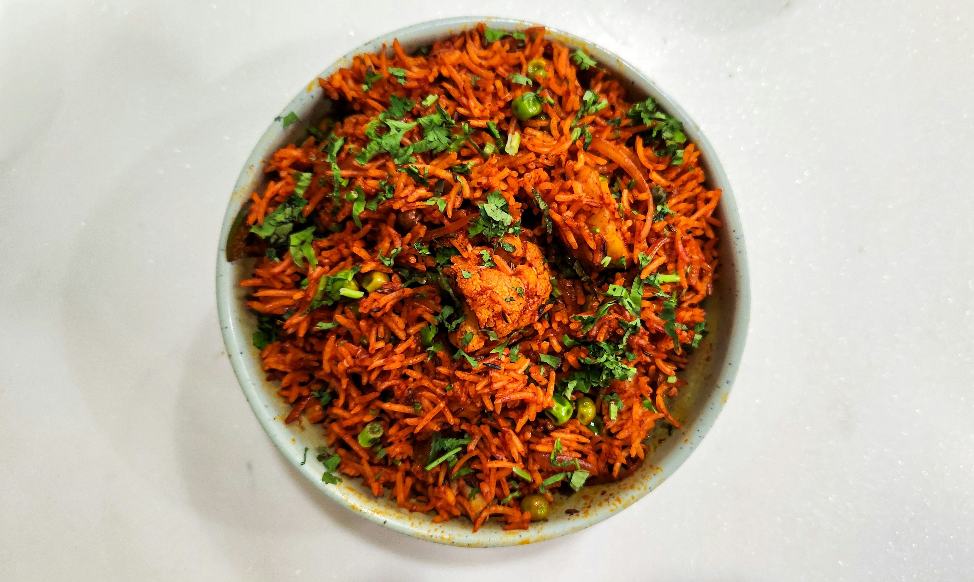 A bowl of red-orange spiced fried rice scattered with chopped coriander