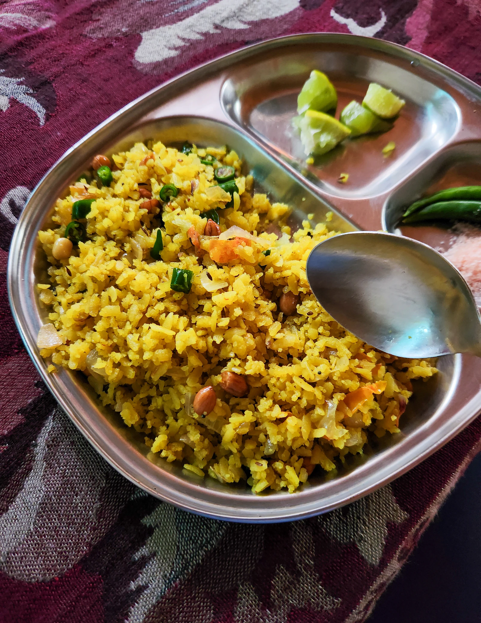 A steel plate of yellow poha with peanuts, green chilli and lemon