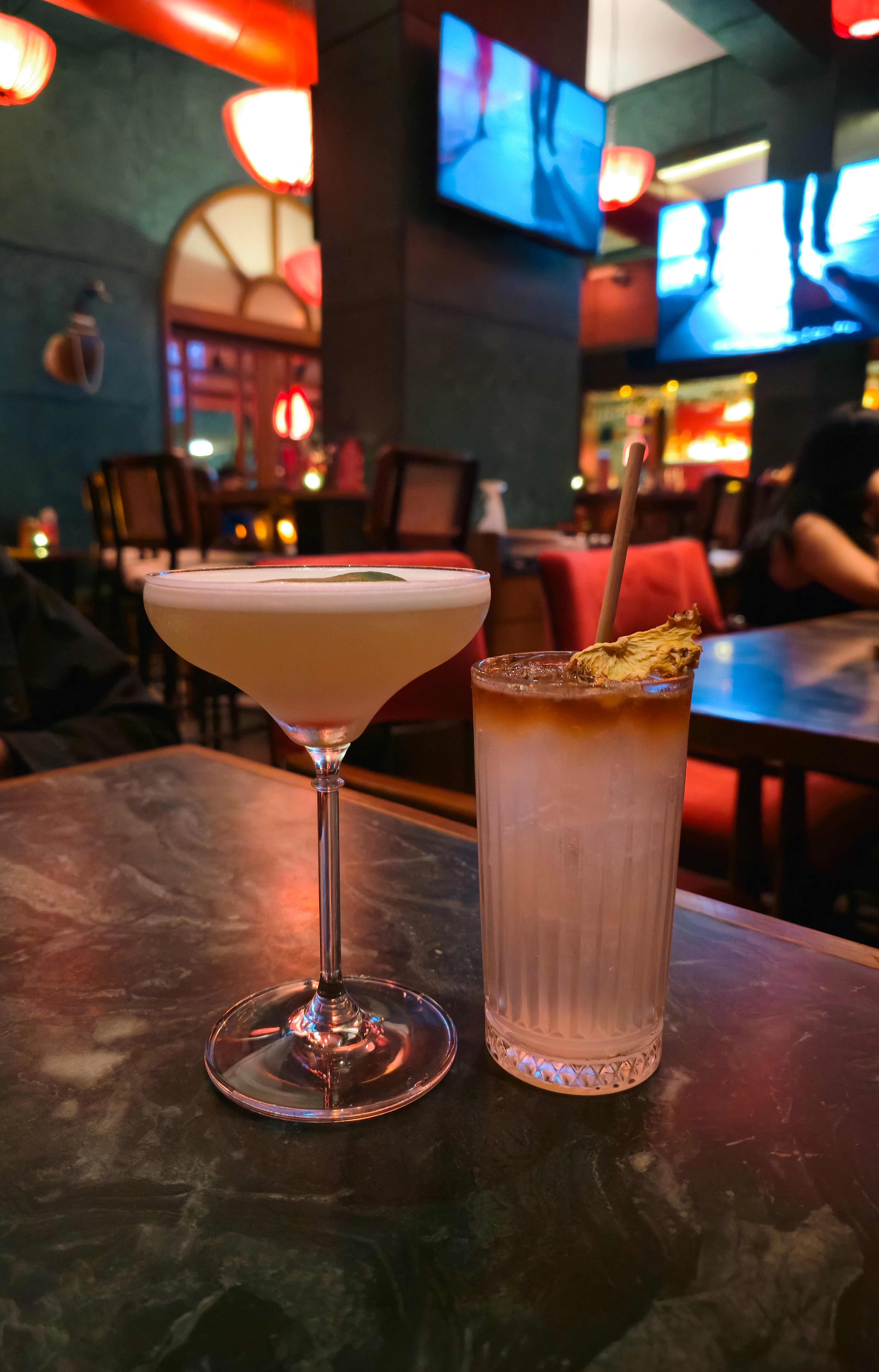 Two cocktails on a marble table in a dim bar