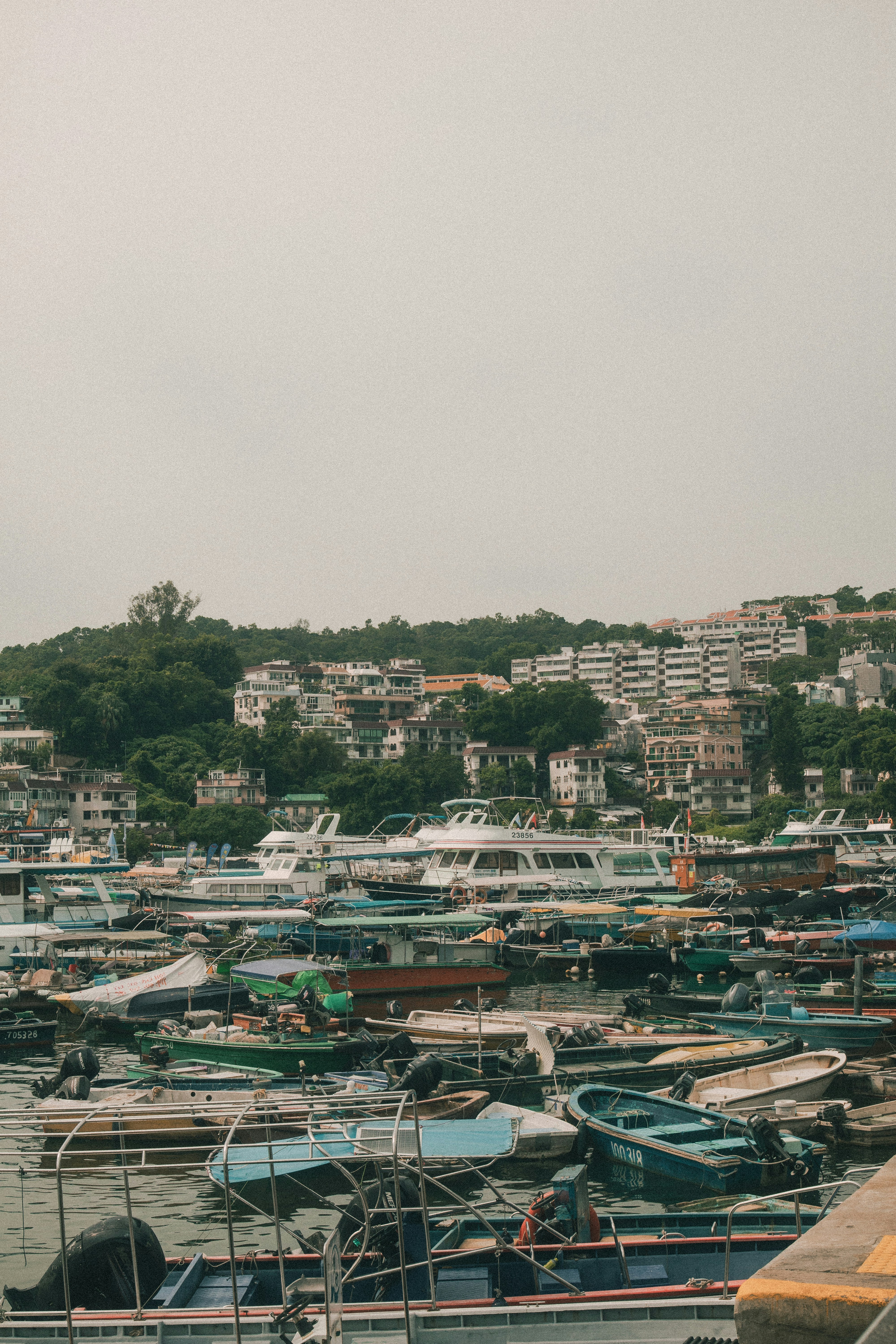 Many small boats moored in a harbor below a hillside with apartment buildings