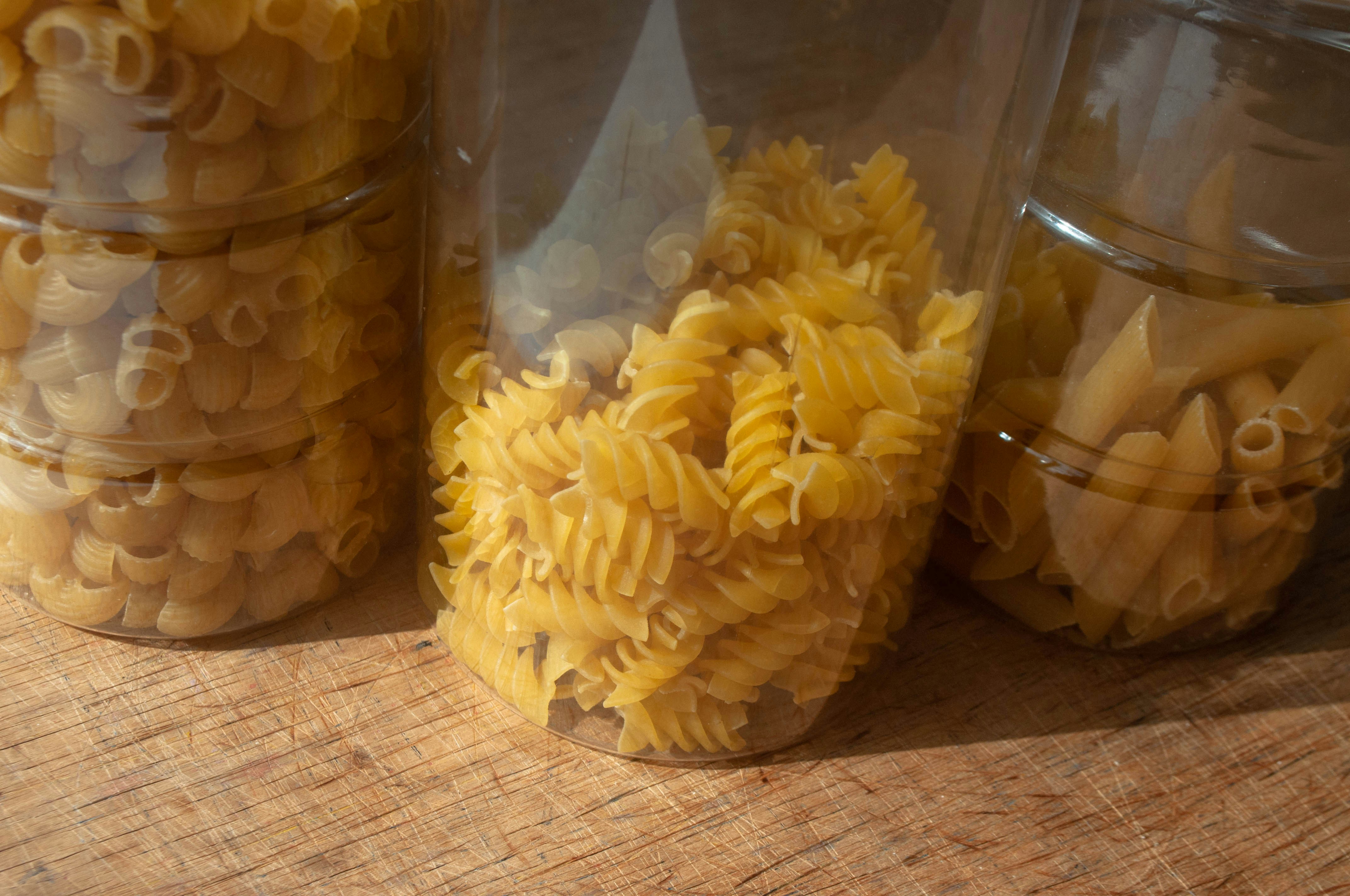Fotomural Three clear plastic containers filled with dry pasta on a wooden surface