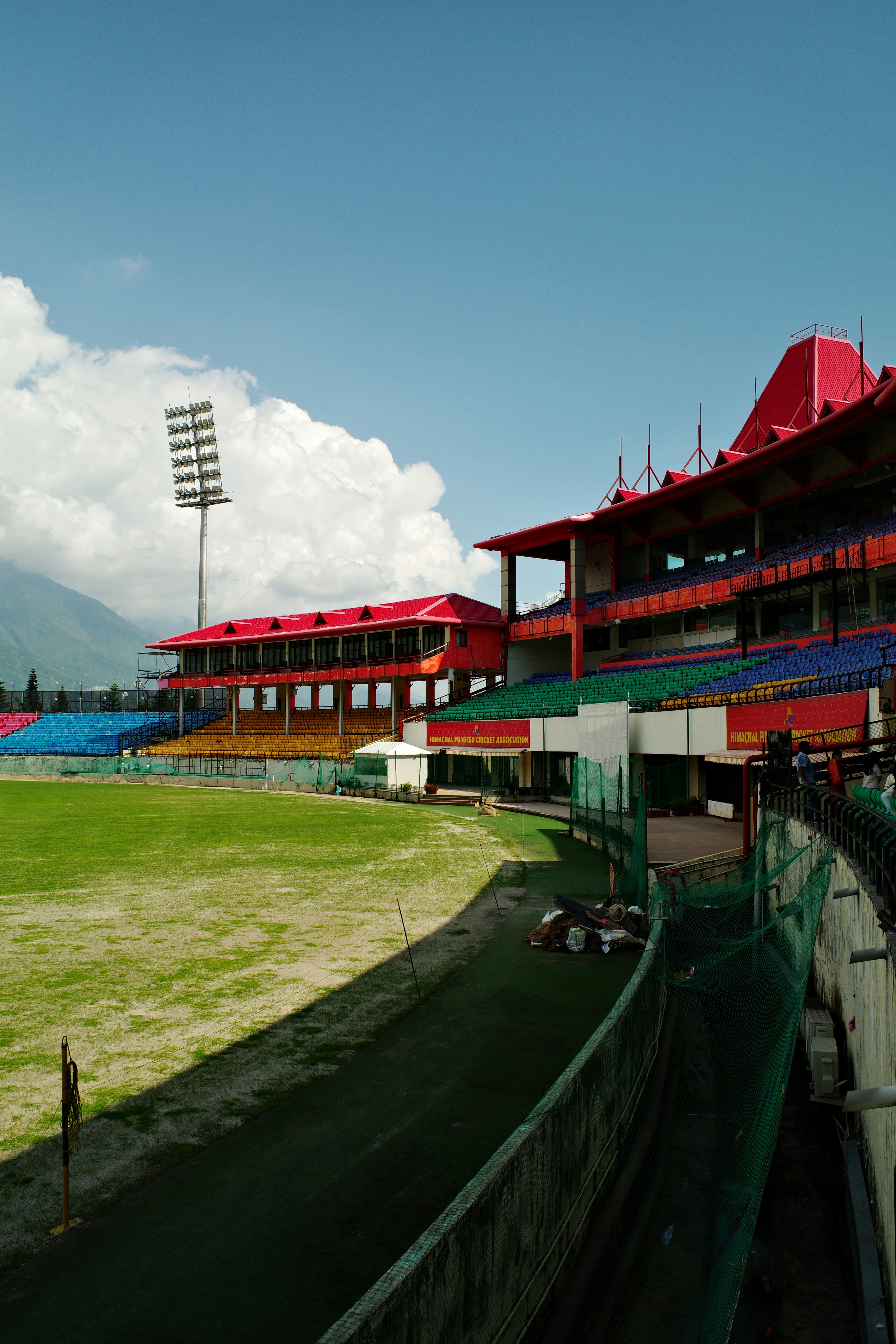 The Himachal Pradesh Cricket Association Stadium with red roofs and colorful seating in Dharamshala