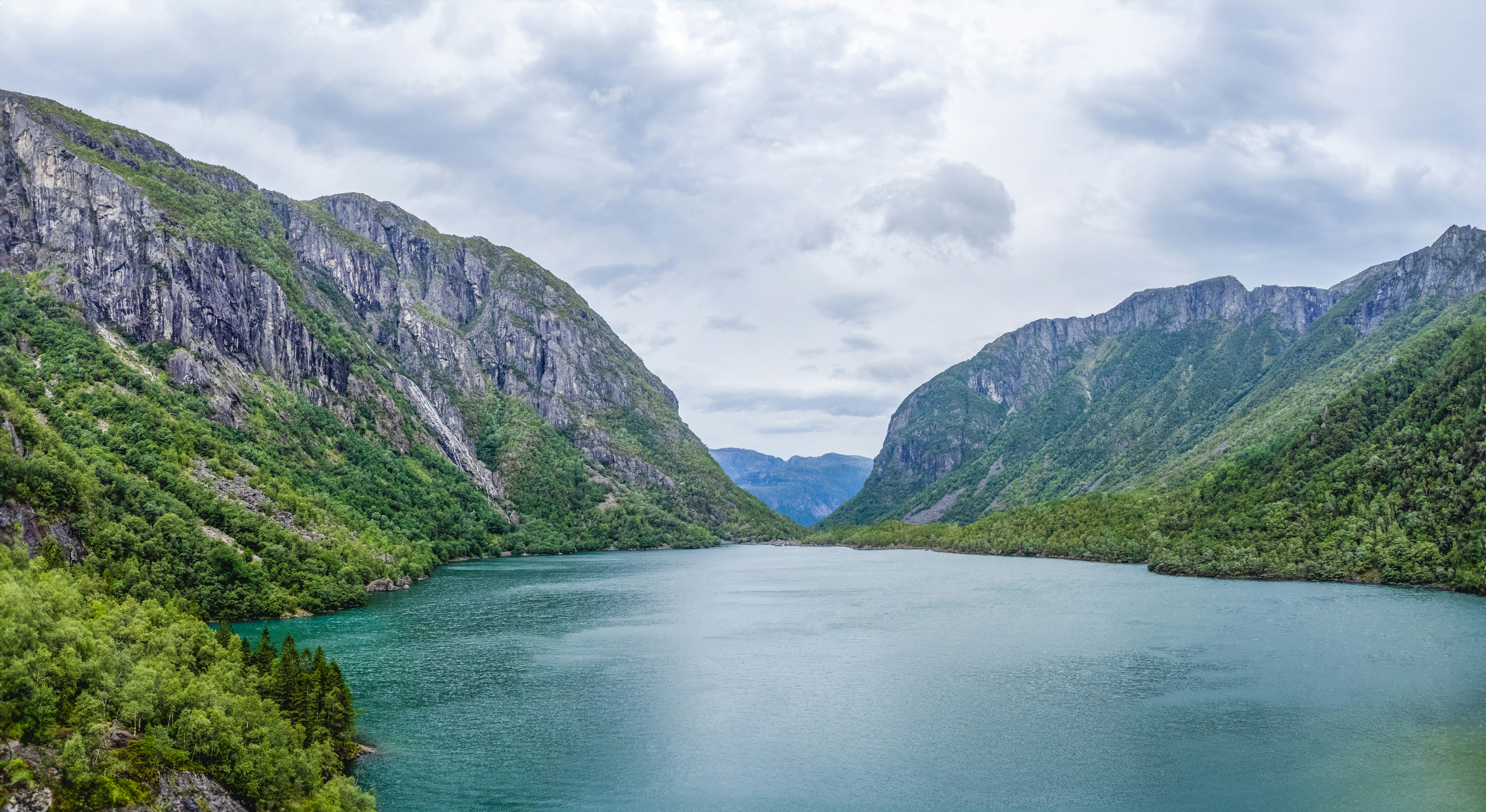 A turquoise lake surrounded by steep green mountains under a cloudy sky