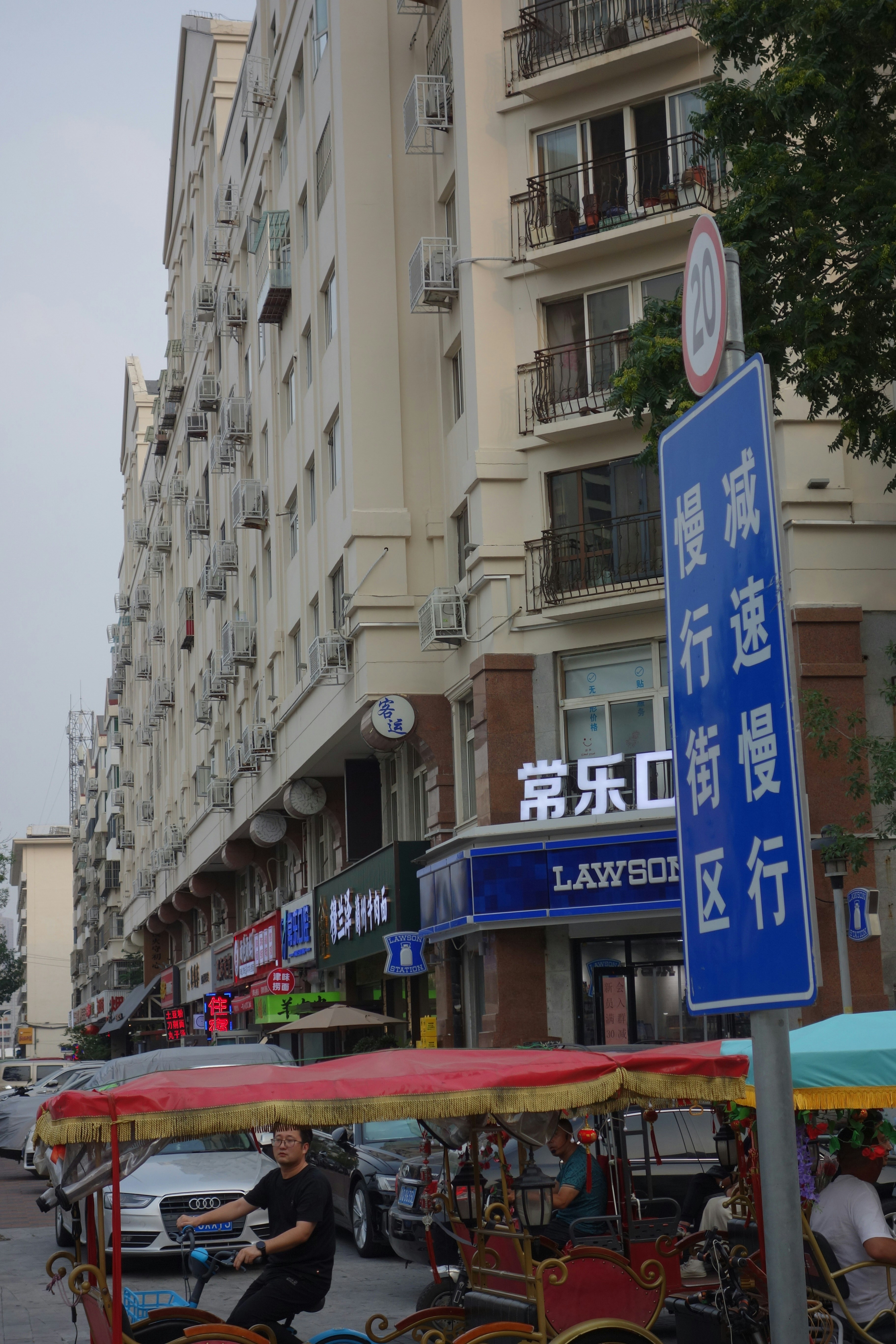 A man cycling a pedicab past a Lawson convenience store on a city street
