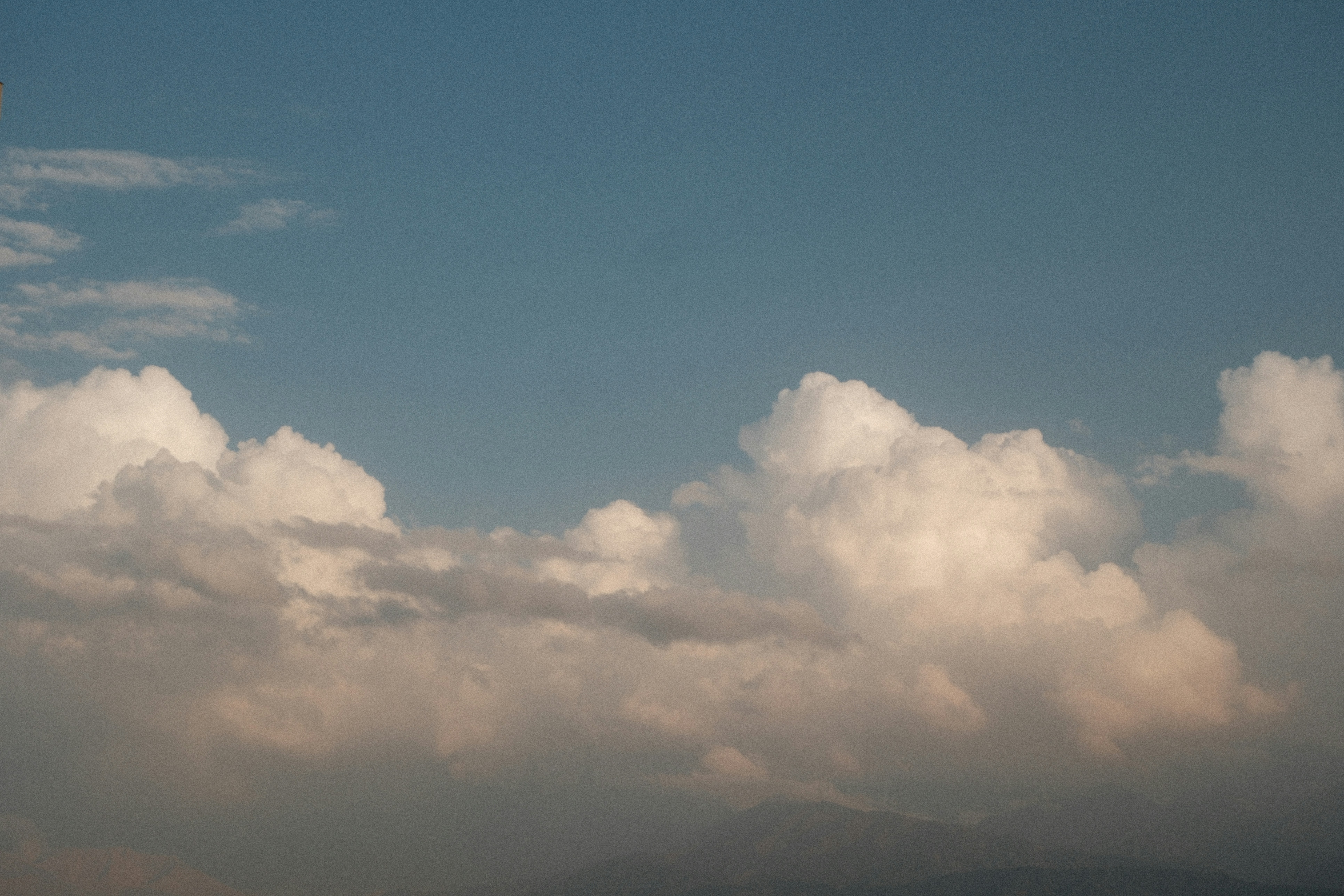 White cumulus clouds drifting above dark mountain silhouettes against a clear blue sky