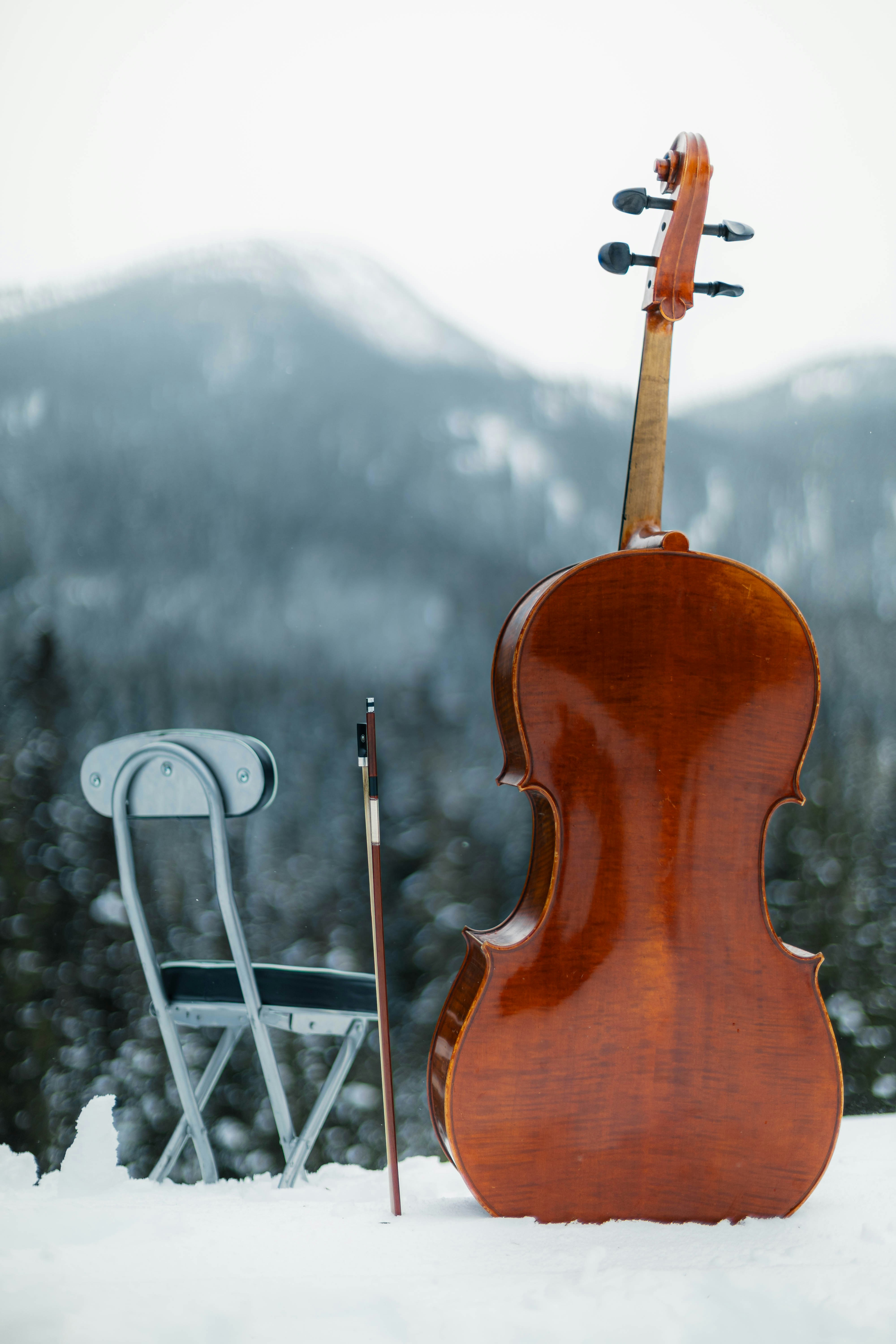 A cello and bow beside a folding chair on a snowy mountain landscape