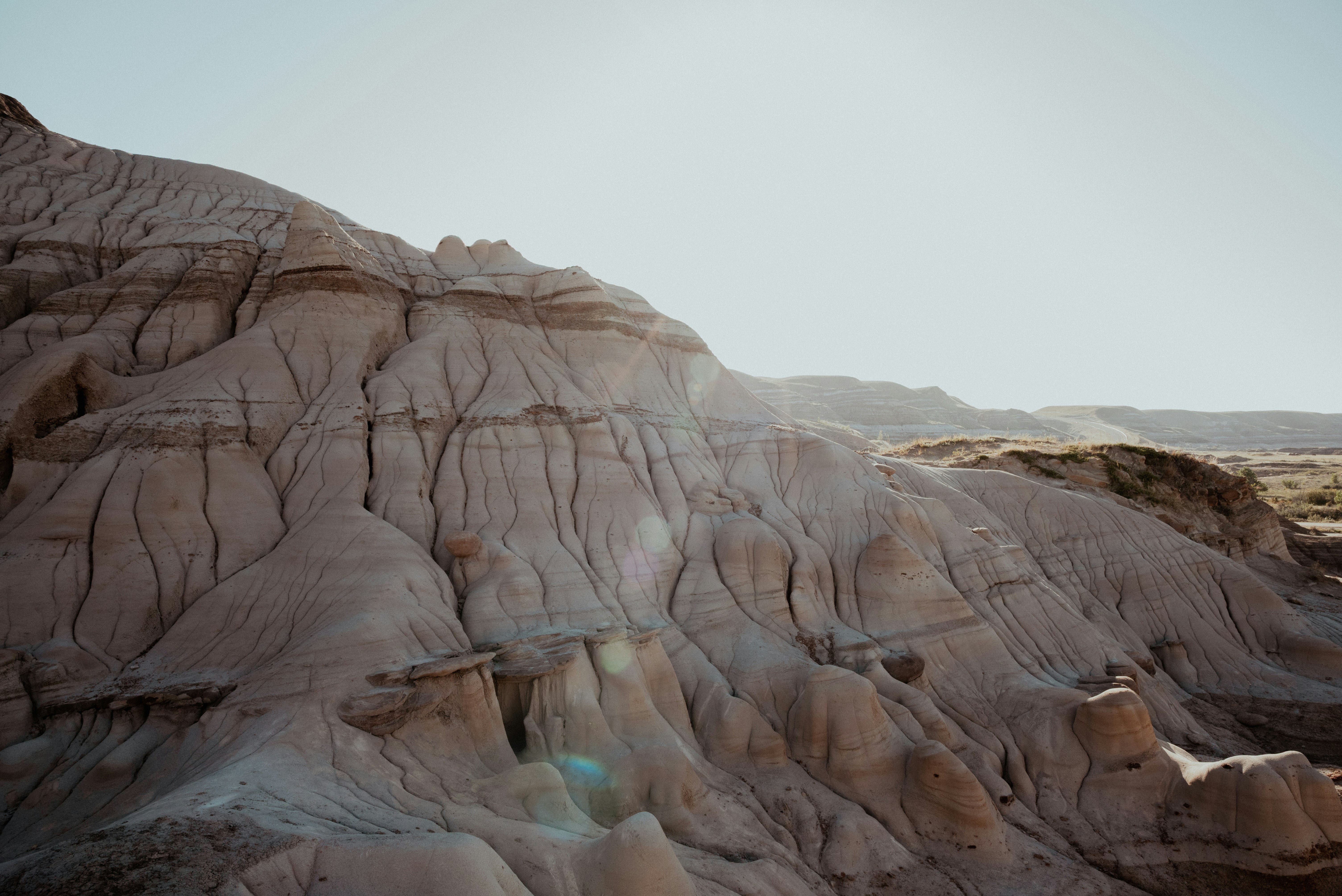 Eroded sandstone hoodoos and ridges under a bright sky with lens flare