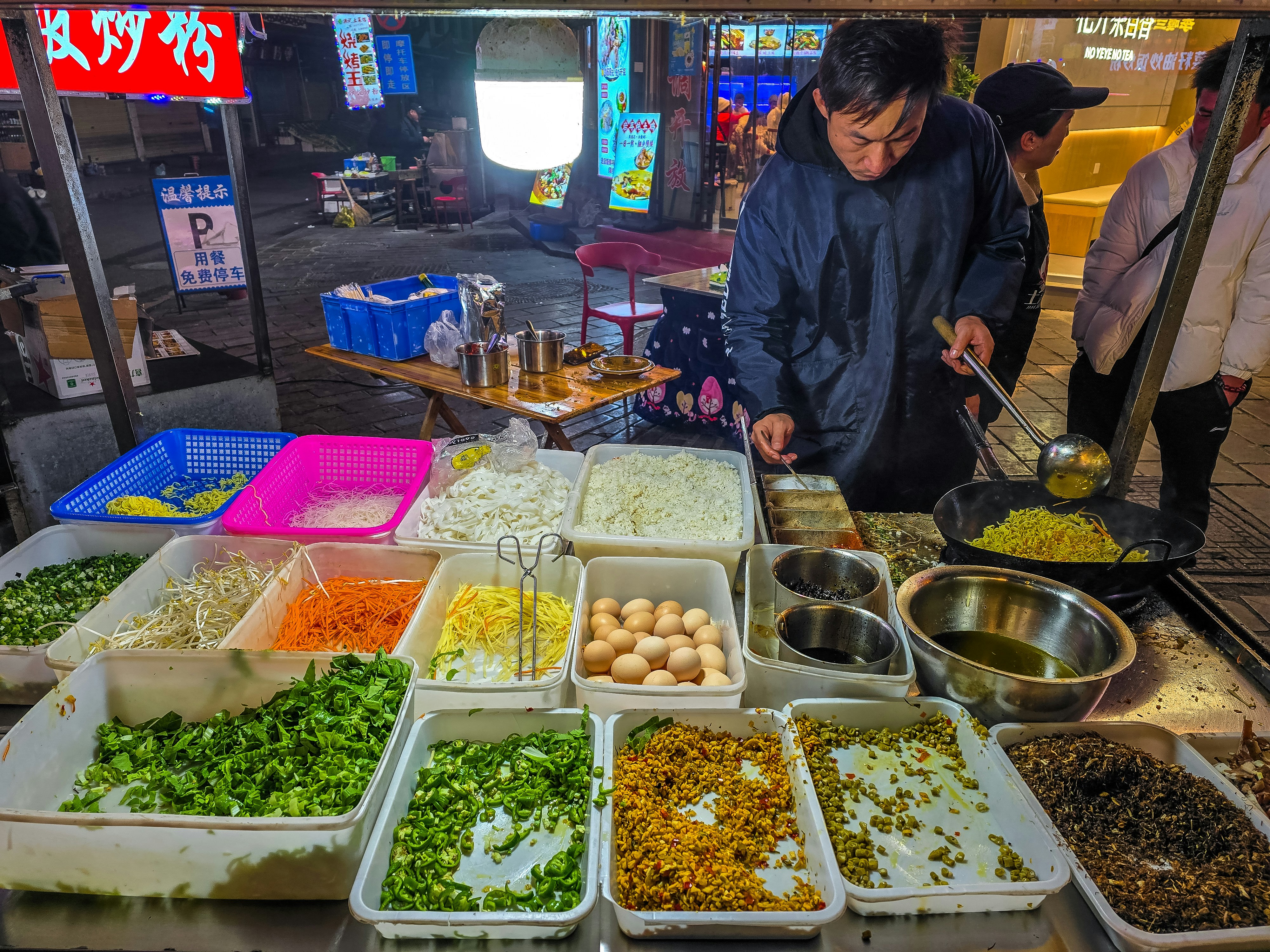 Street vendor with trays of noodle toppings and chopped vegetables