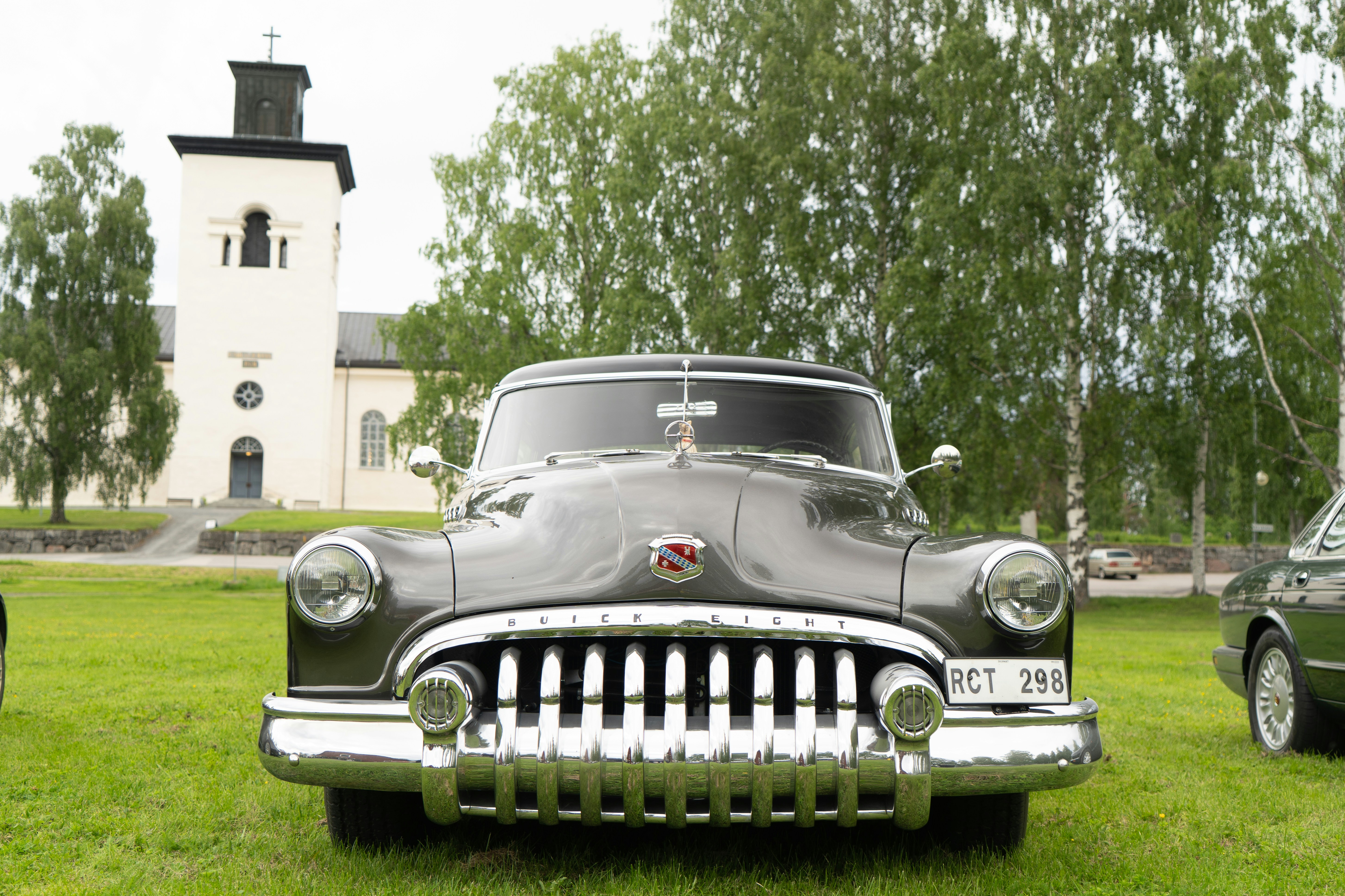 A vintage grey Buick Eight car parked on a lawn before a white church