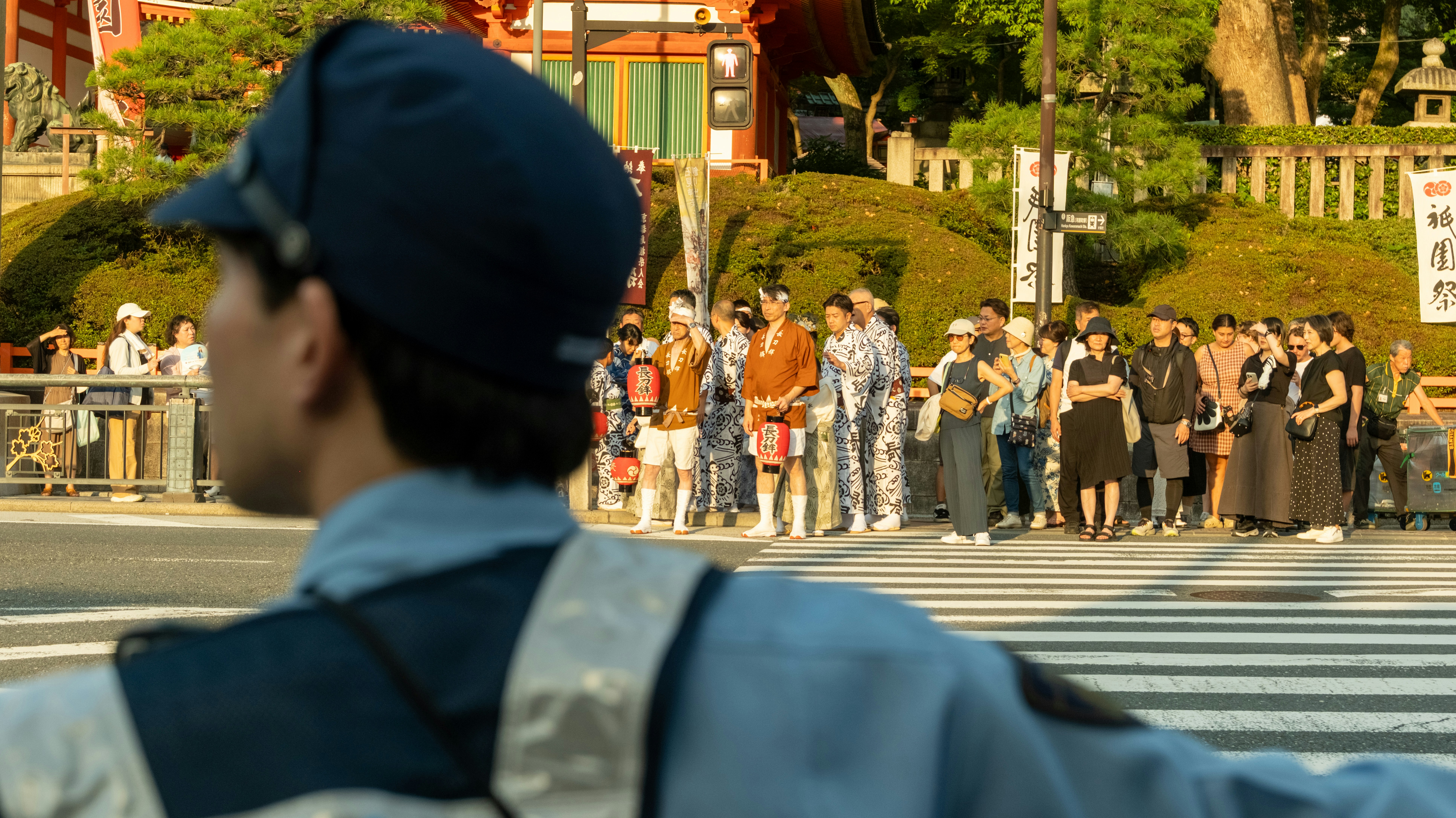 A police officer directing traffic as people wait at a crosswalk in Kyoto