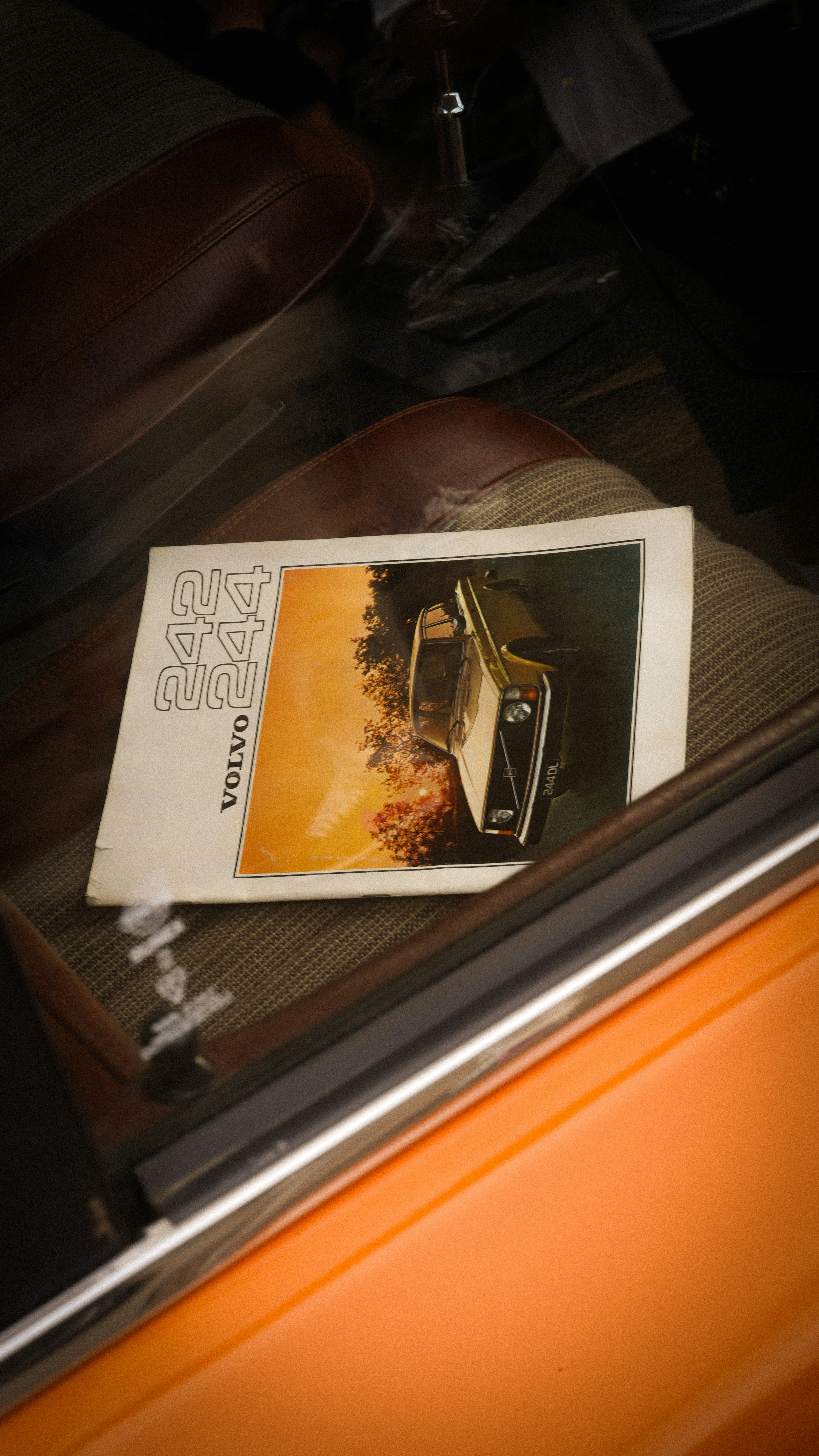 A vintage Volvo brochure on a textured car seat inside an orange car