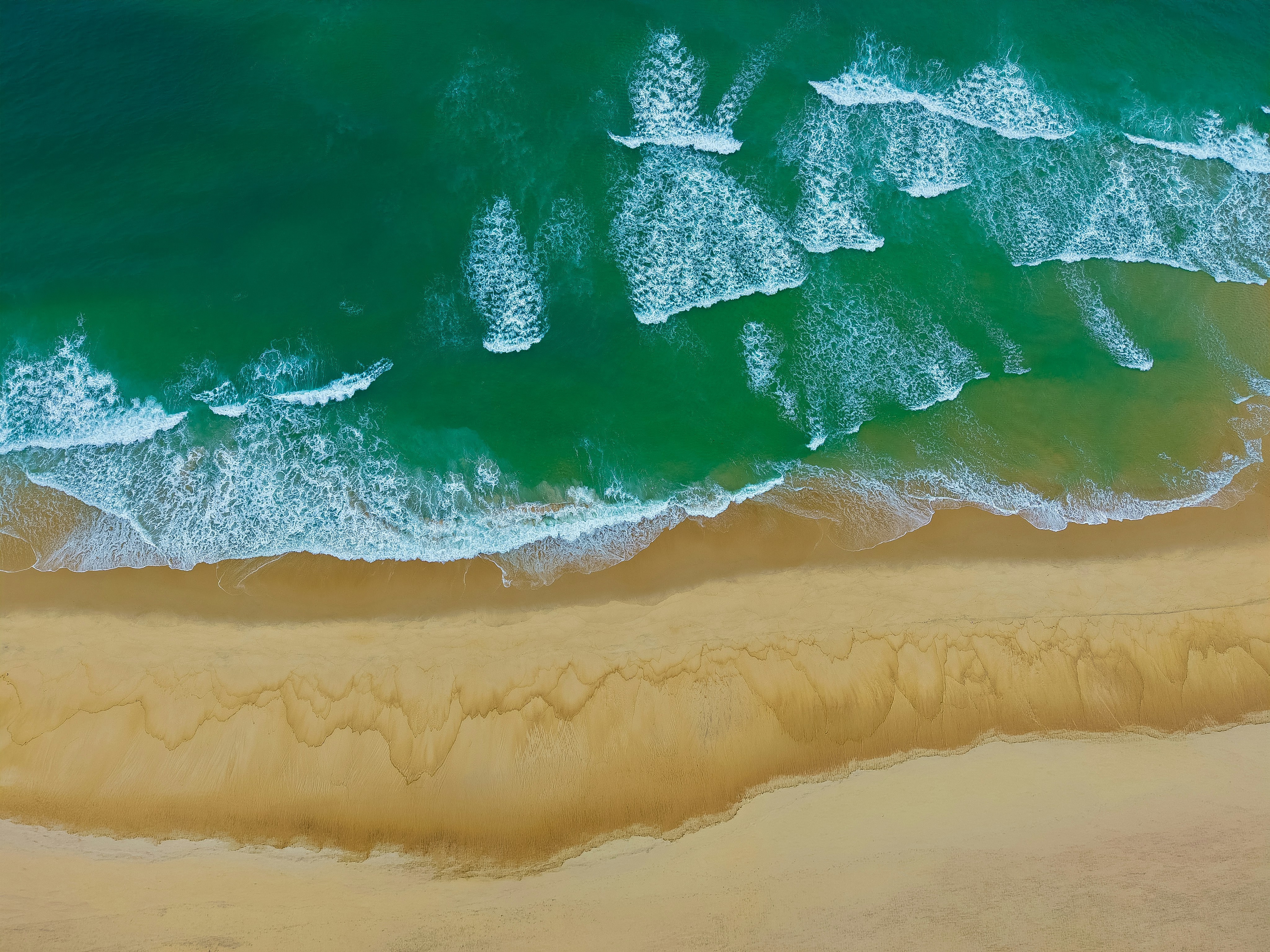 An aerial view of turquoise ocean waves breaking onto a sandy beach