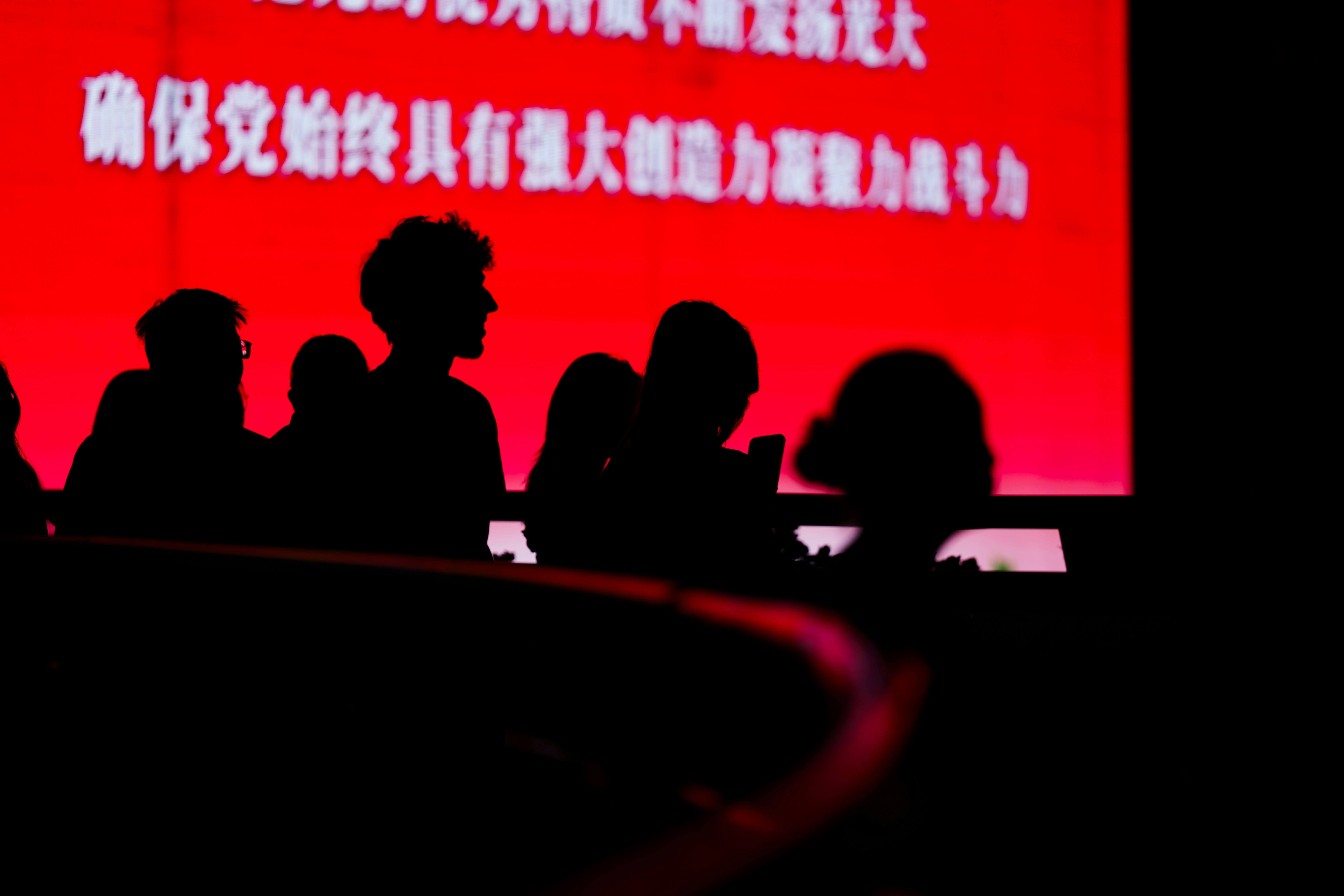 Silhouettes of people in front of a bright red screen with white text