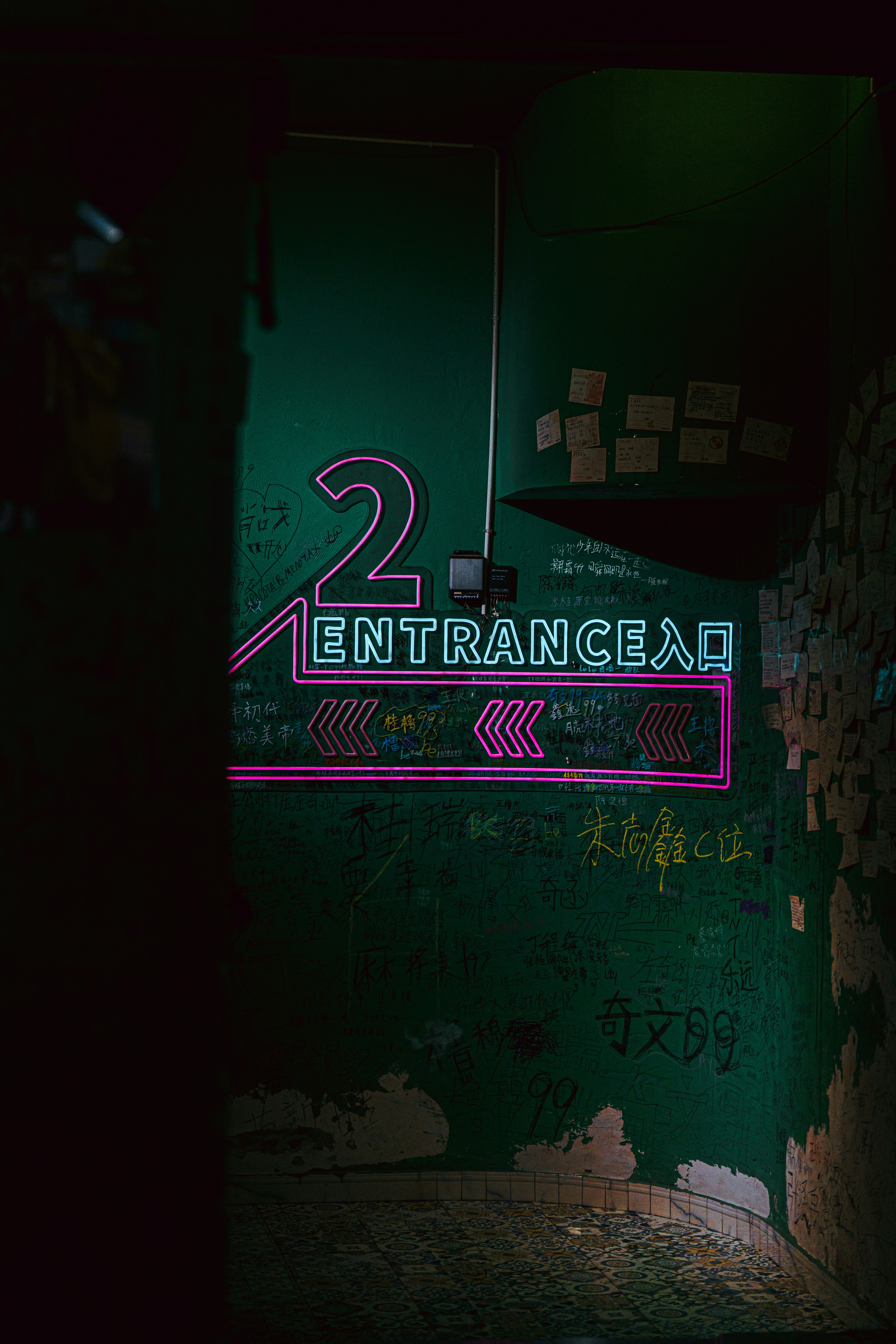 A neon sign reading "2 ENTRANCE" on a dark green wall covered in graffiti