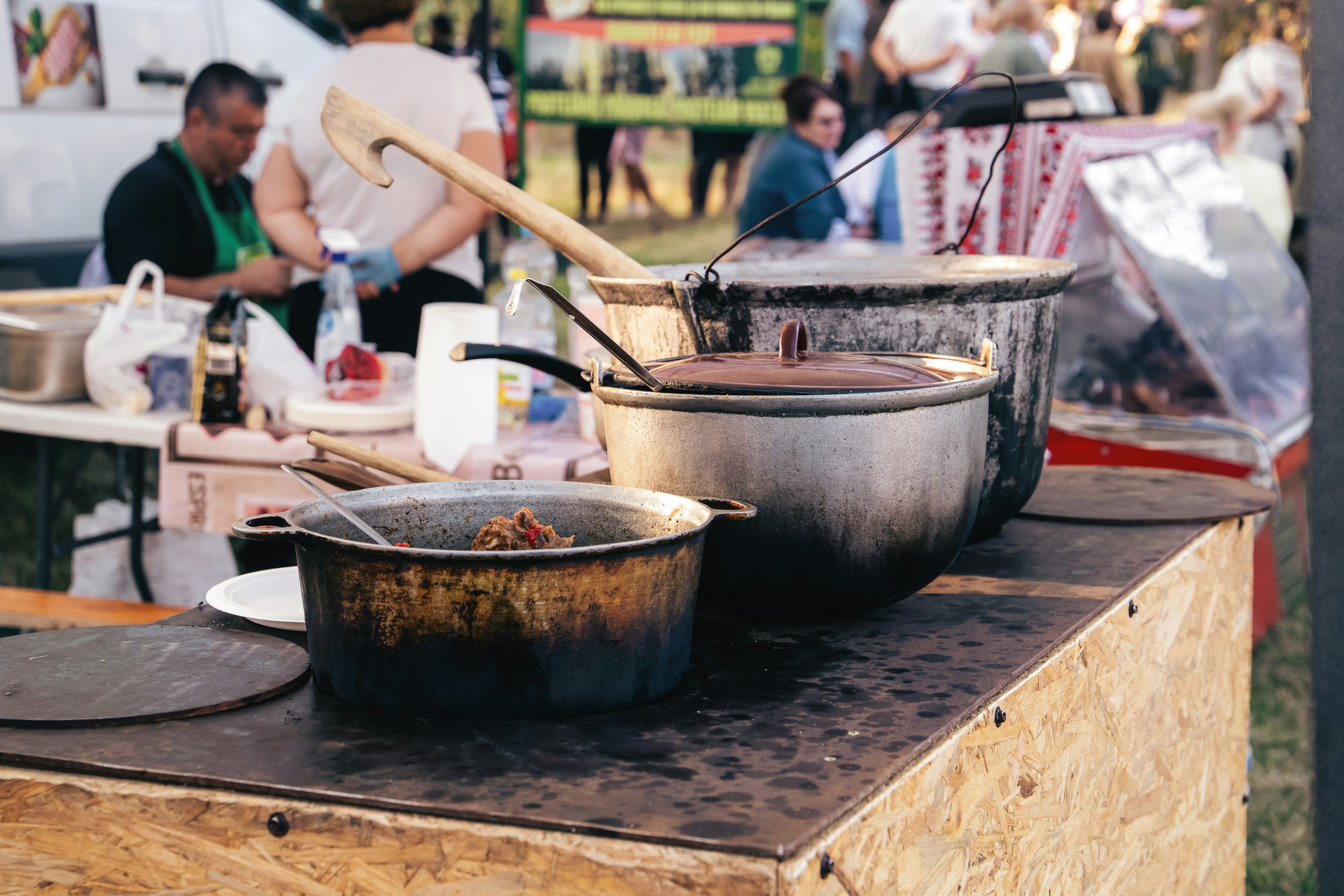 Three large metal cooking pots on a wooden outdoor food stall counter