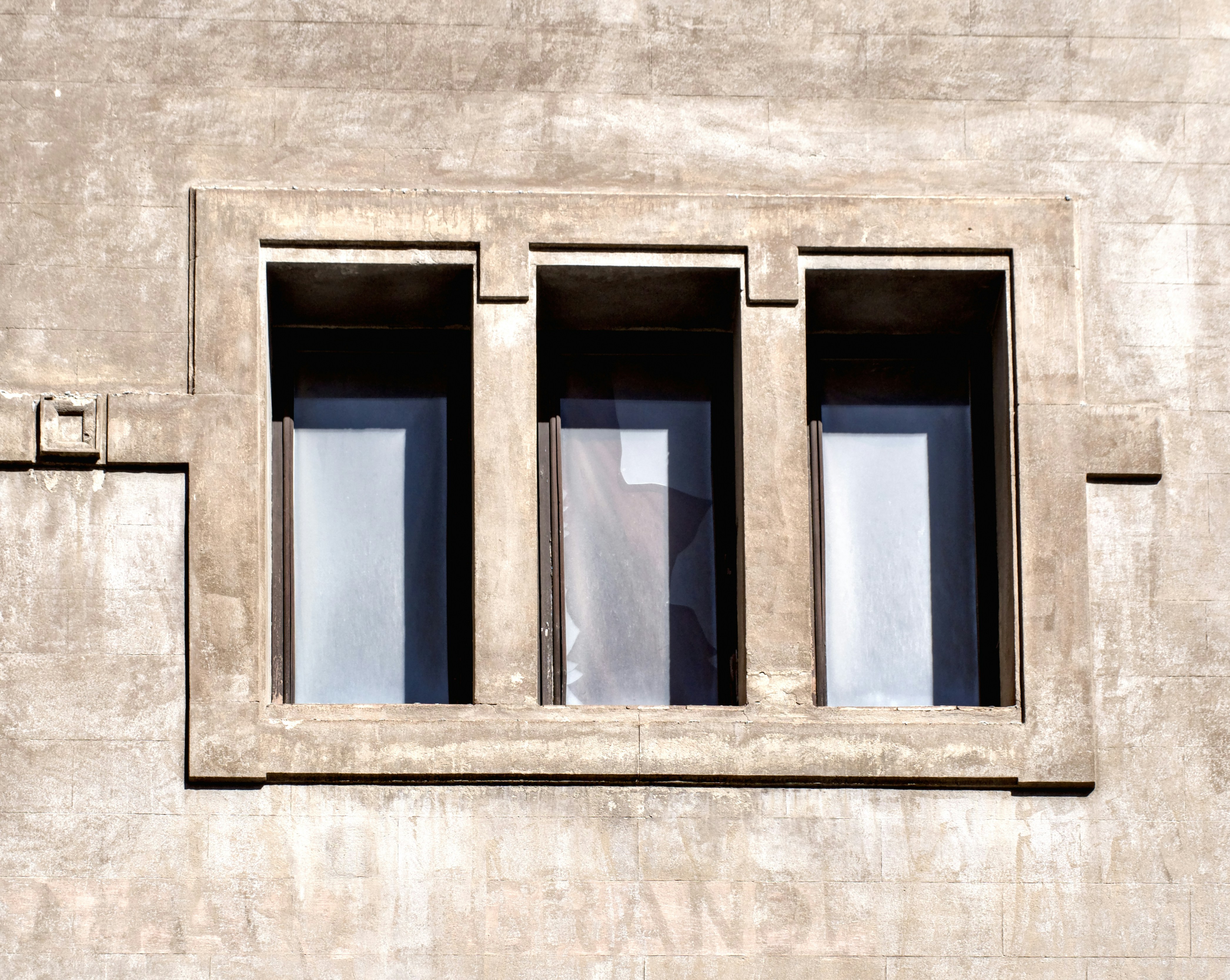 Three rectangular windows set into a weathered beige concrete wall
