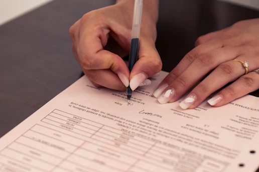 A person signing a document with a black pen on a dark table