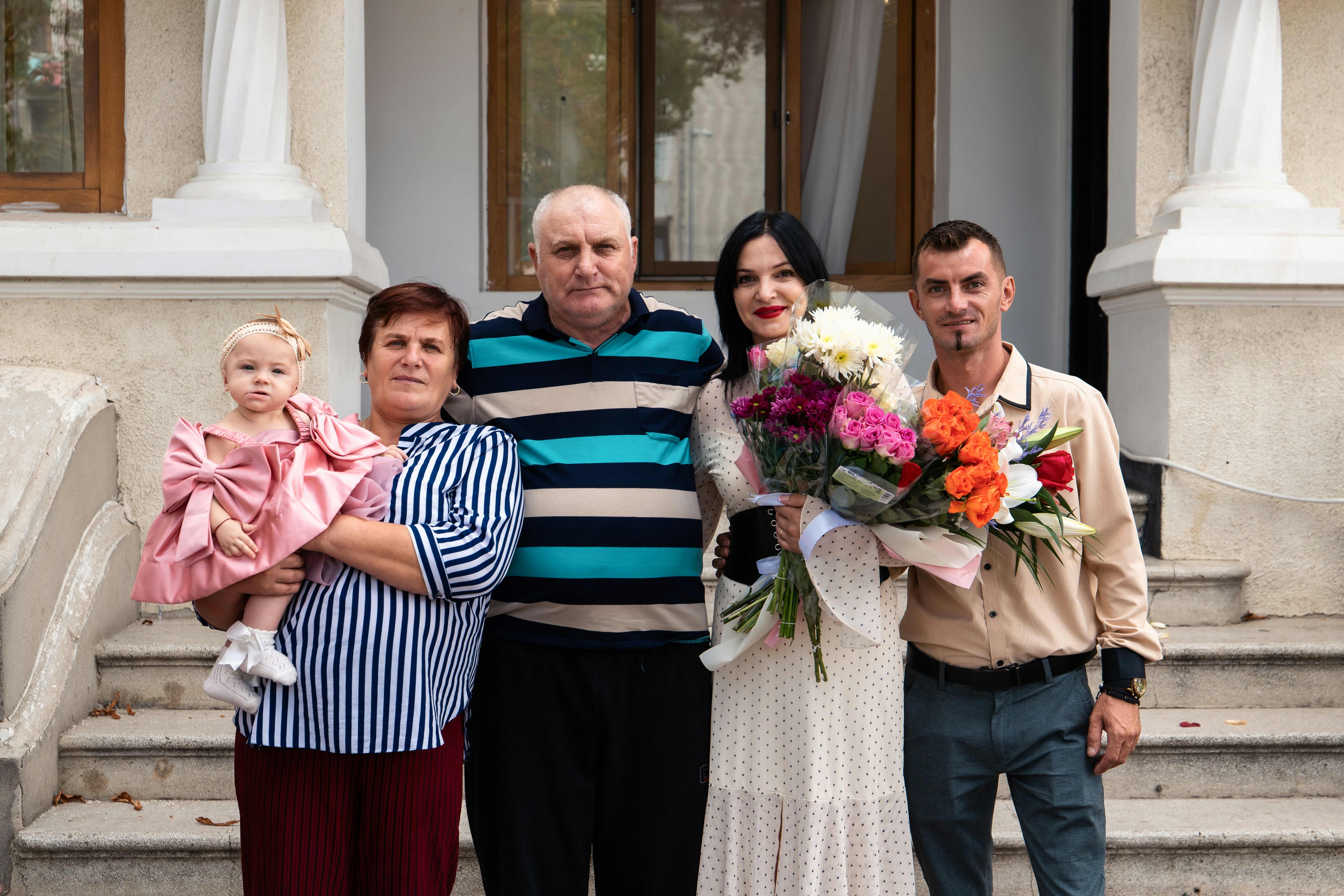 Eine Familie auf Steinstufen, zwei Erwachsene mit einem Baby und einem Blumenstrauß