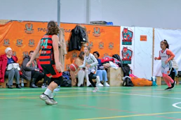 Three children playing basketball on an indoor court with spectators in the background