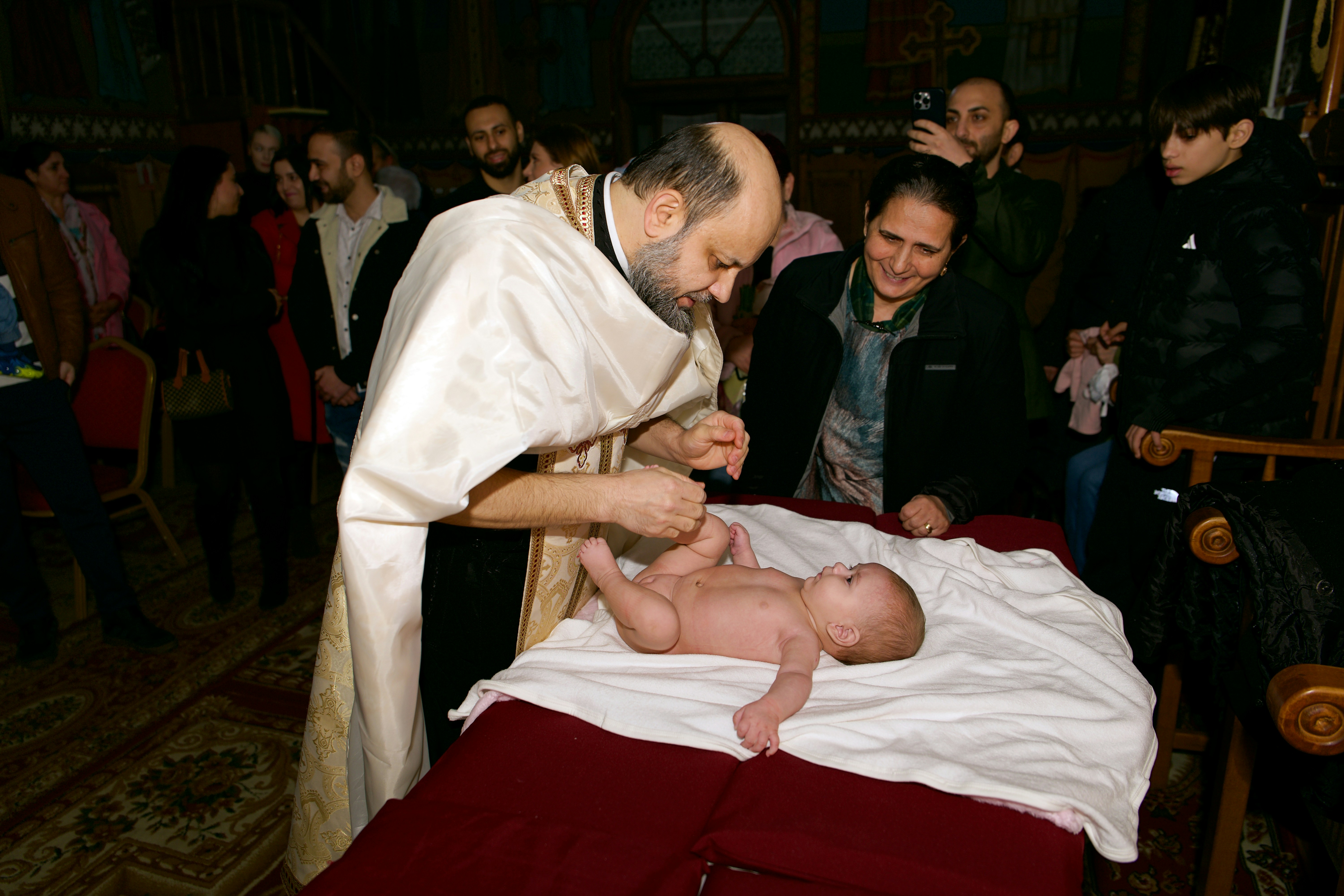 A priest in white vestments touching the foot of a baby during a baptism